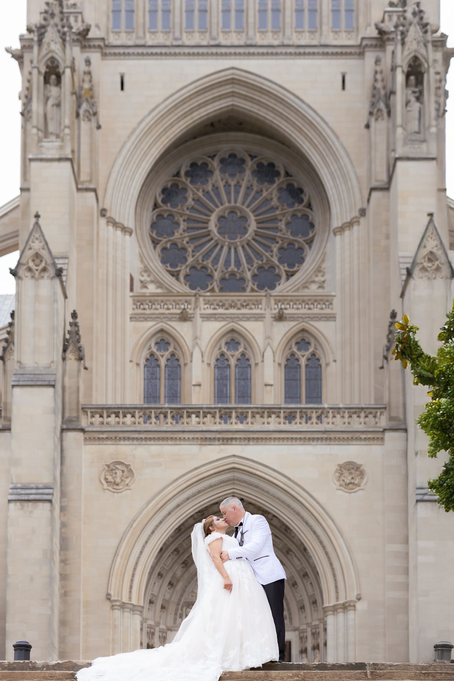 A couple embraces on the steps of Washington National Cathedral with its stunning Gothic architecture and rose window above.
