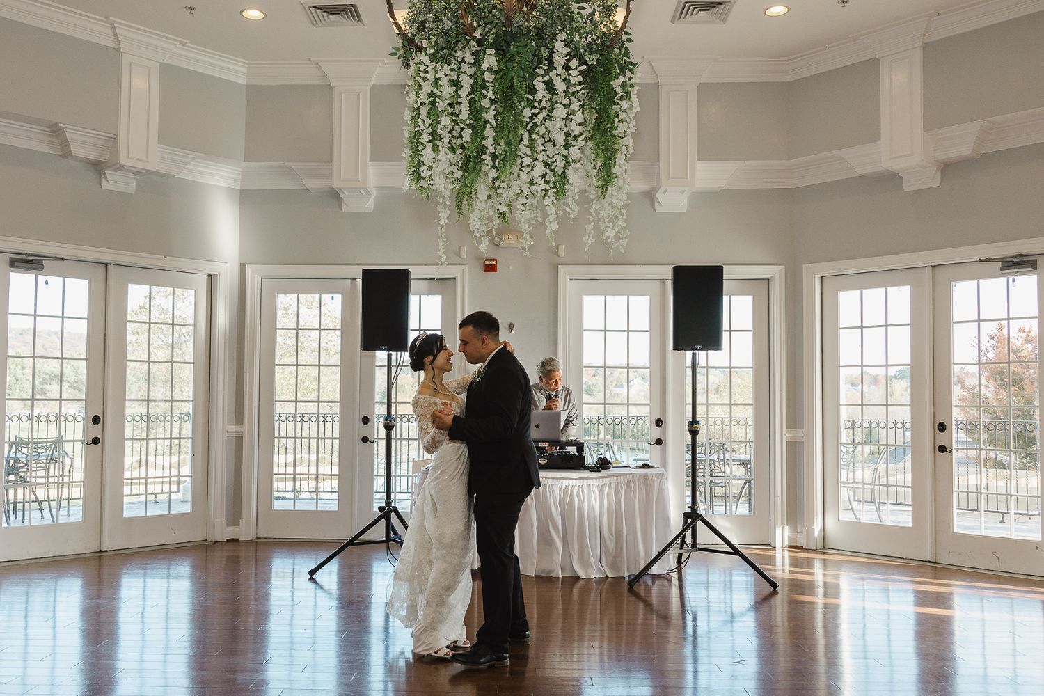 A couple shares their first dance in an elegant white rotunda room with hanging greenery and French doors.