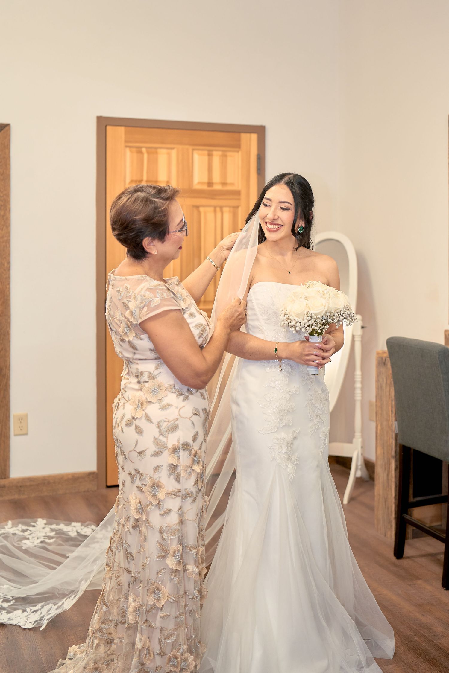 A touching moment between a bride in a white lace gown and woman in a floral dress during wedding preparations.
