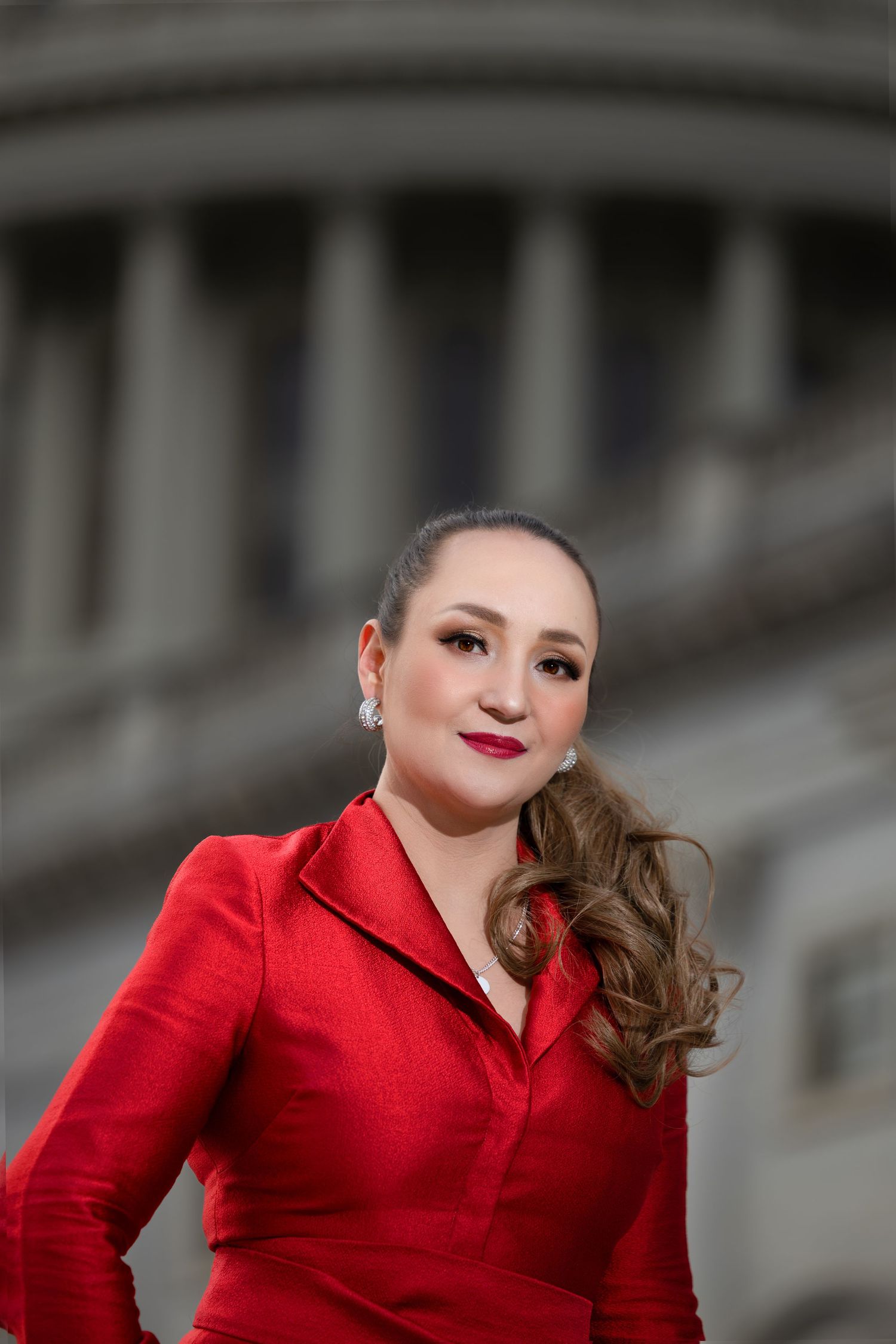 Portrait of woman in red blazer with glamorous makeup against Capitol building backdrop.