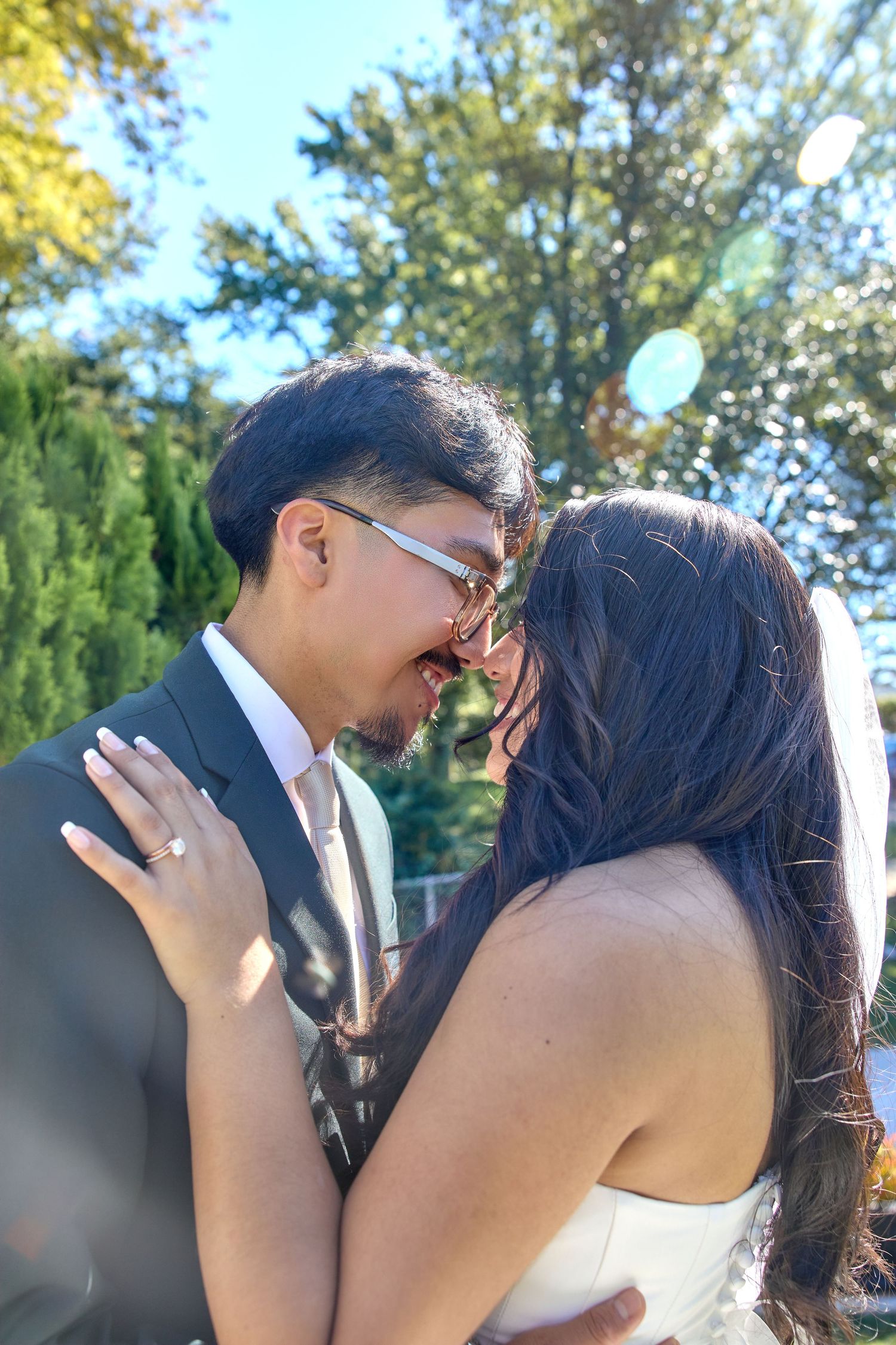 A romantic outdoor wedding kiss between a couple with autumn trees in the background.