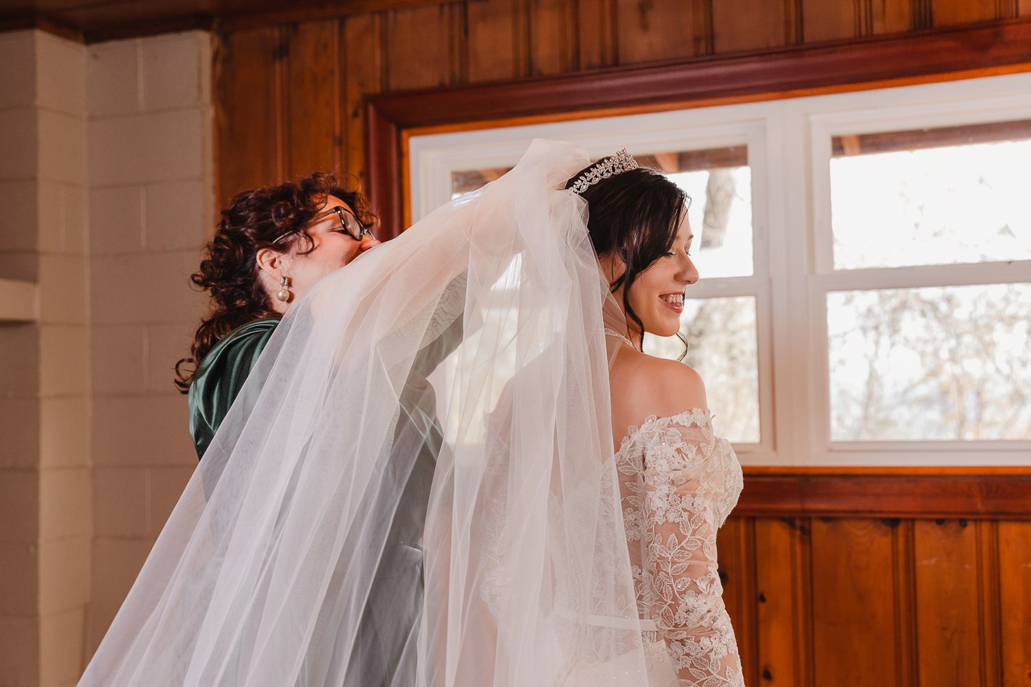 A bride and bridesmaids share an emotional moment while getting ready in a warmly lit room.