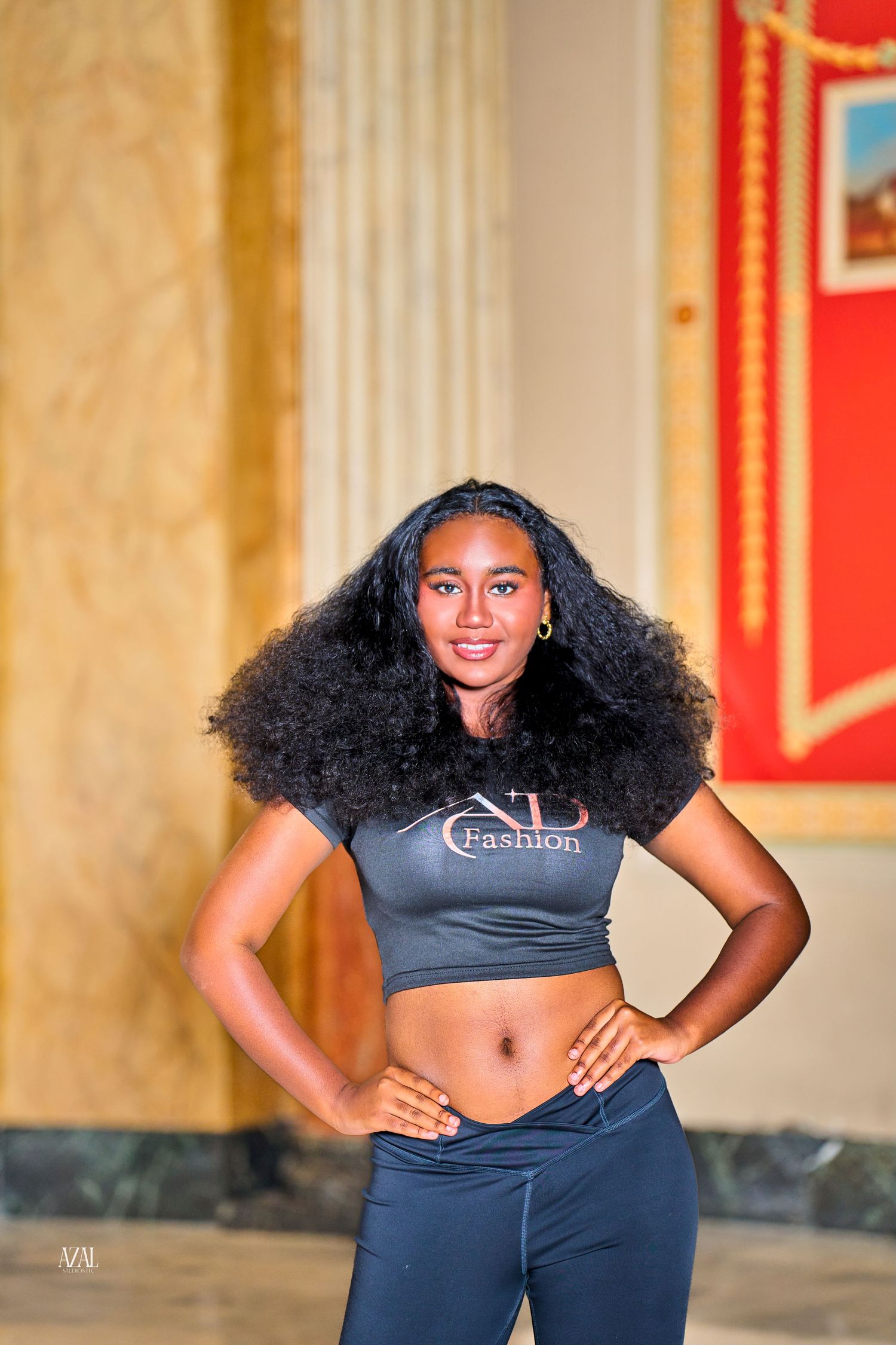 Young woman with voluminous natural hair in black VD Fashion crop top poses in elegant marble hall.
