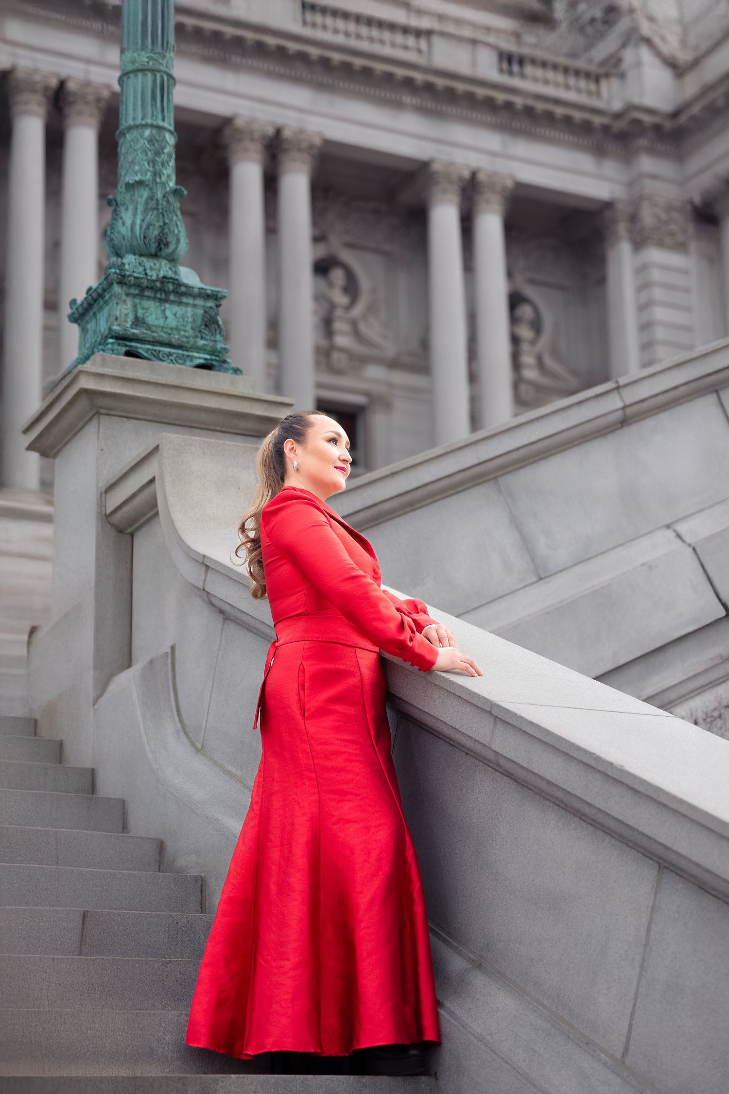 Striking red coat dress photographed on classical building steps with ornate architecture.