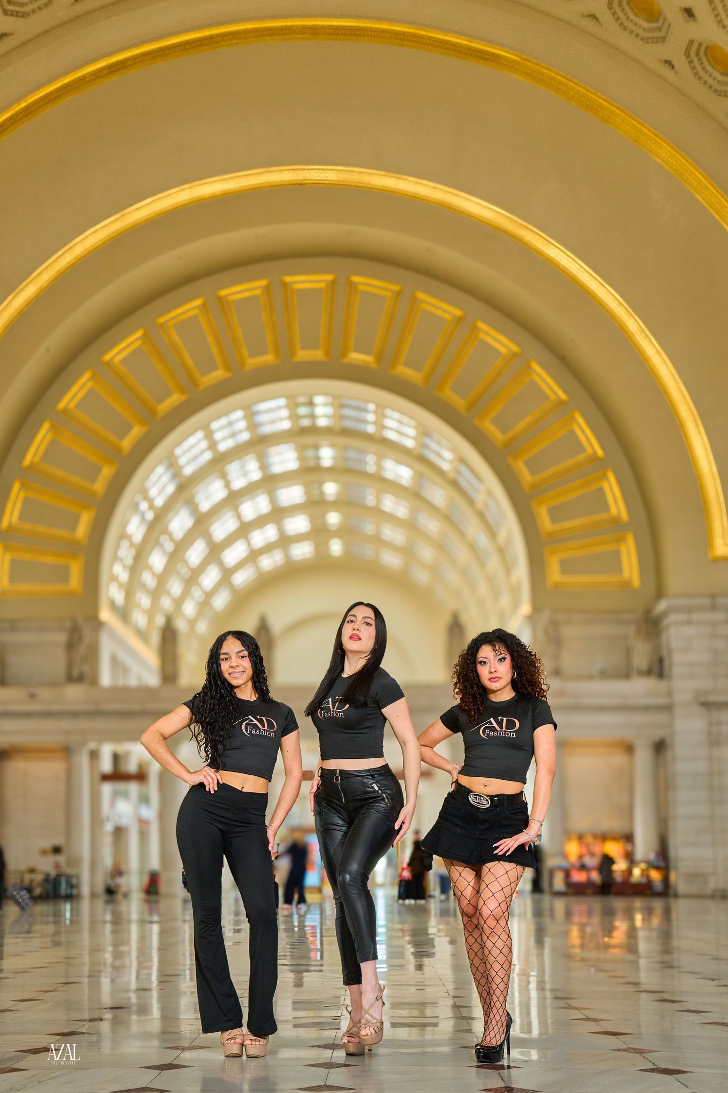 Three women in matching black ND Fashion outfits pose under golden arched ceiling of Union Station.