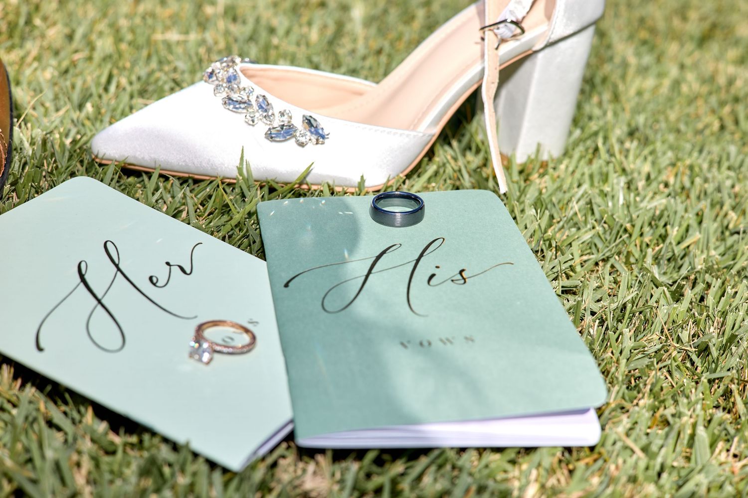 Elegant wedding rings photographed with mint green cards and shoes on grass.