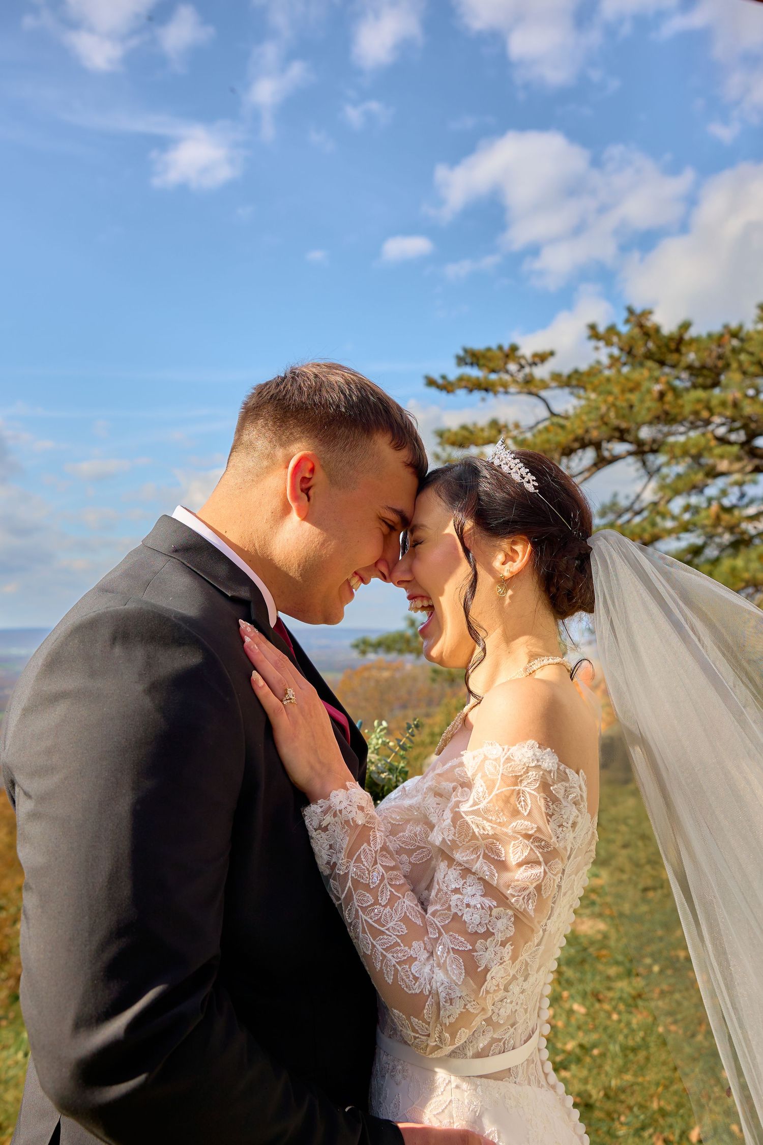 Scenic outdoor wedding photography session with couple in formal attire against blue sky and natural landscape.