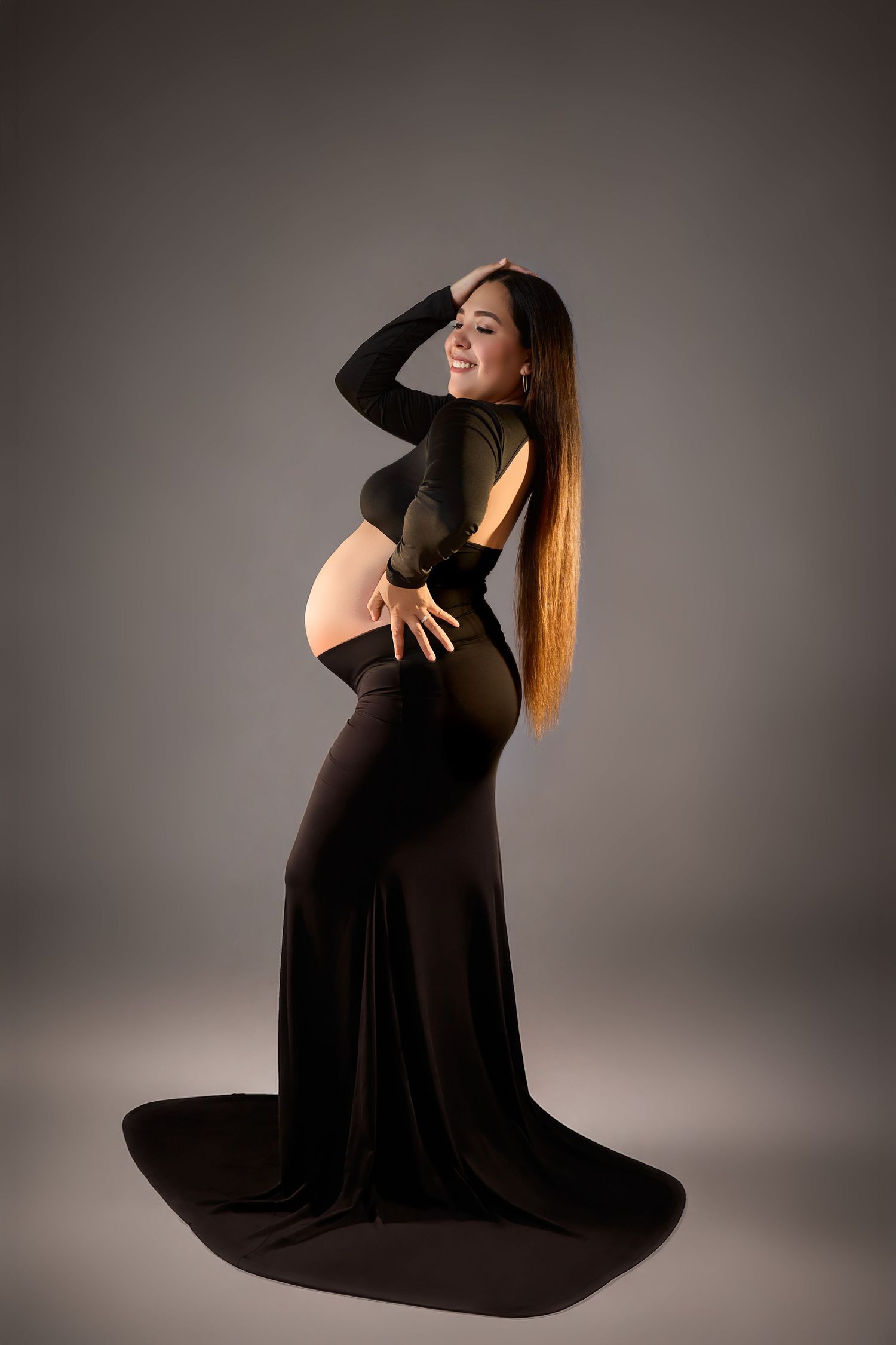 Pregnant woman in elegant black crop top and long skirt posing gracefully in a professional maternity photo shoot.