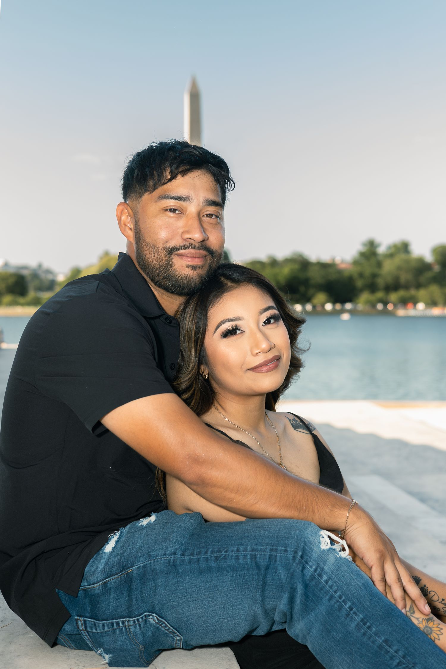 A couple shares a tender moment by the waterfront with the Washington Monument visible in the background.