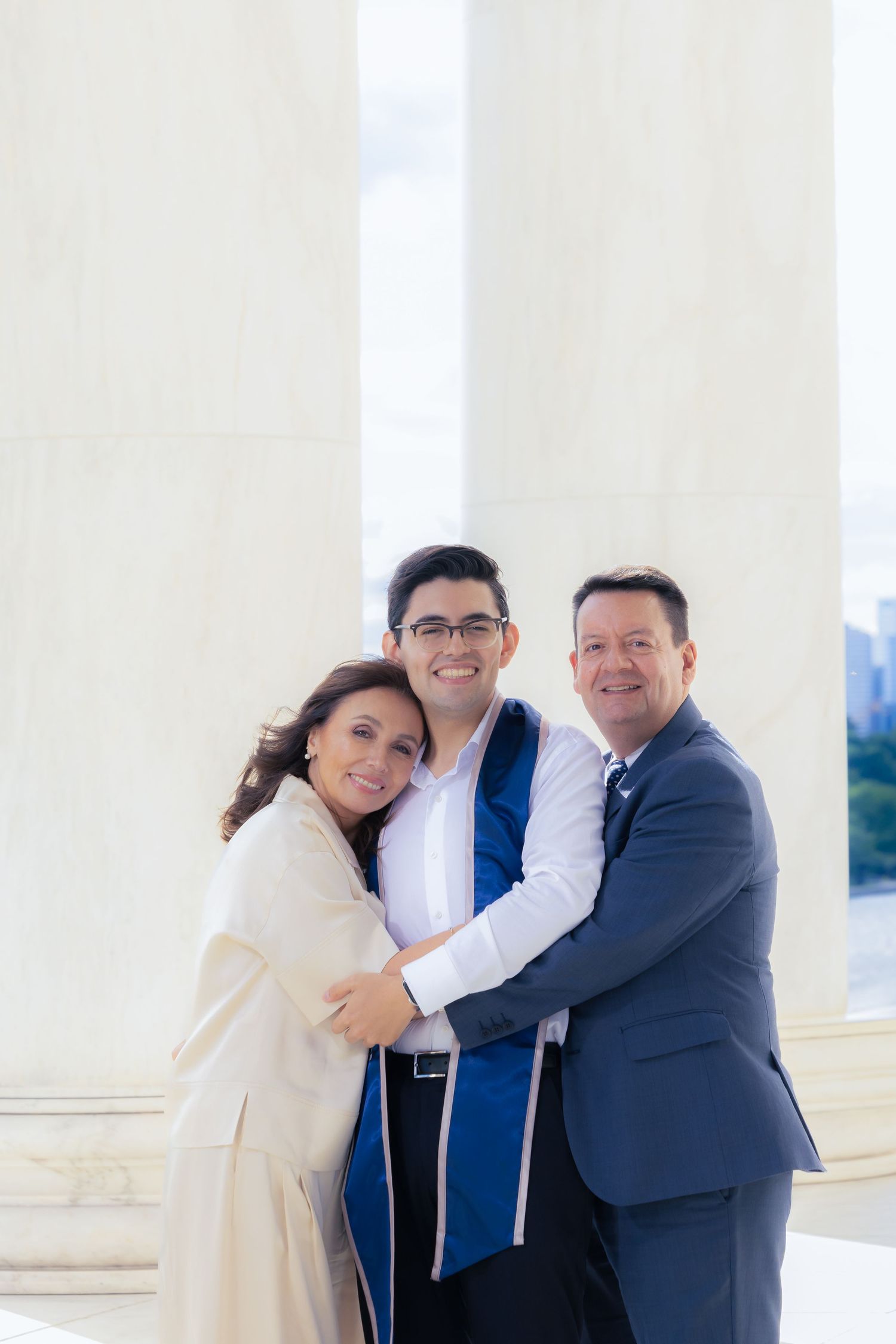 Graduate in blue regalia poses with family members in formal attire near white columns.