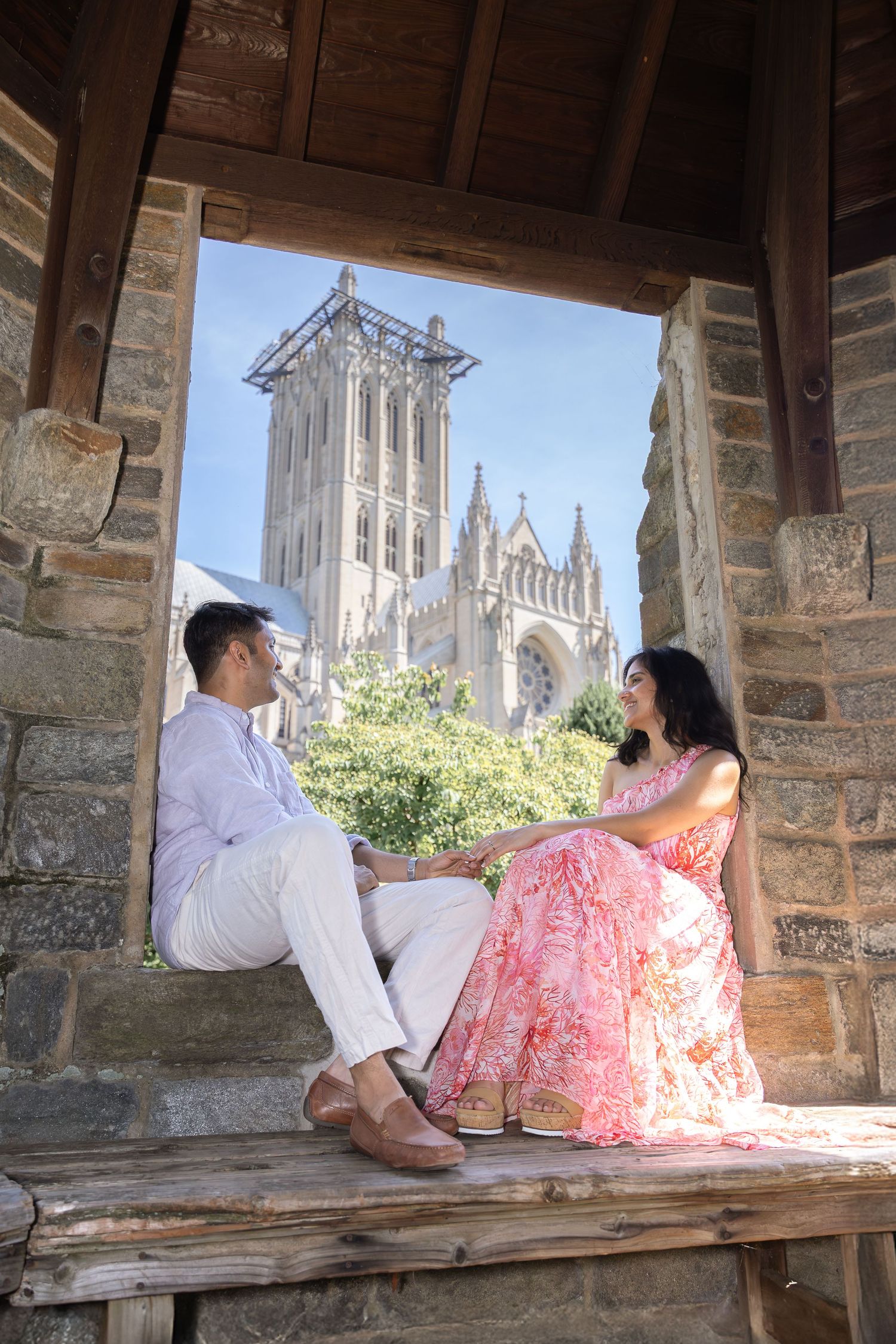 A couple sits together in a stone archway overlooking a Gothic church spire on a sunny afternoon.