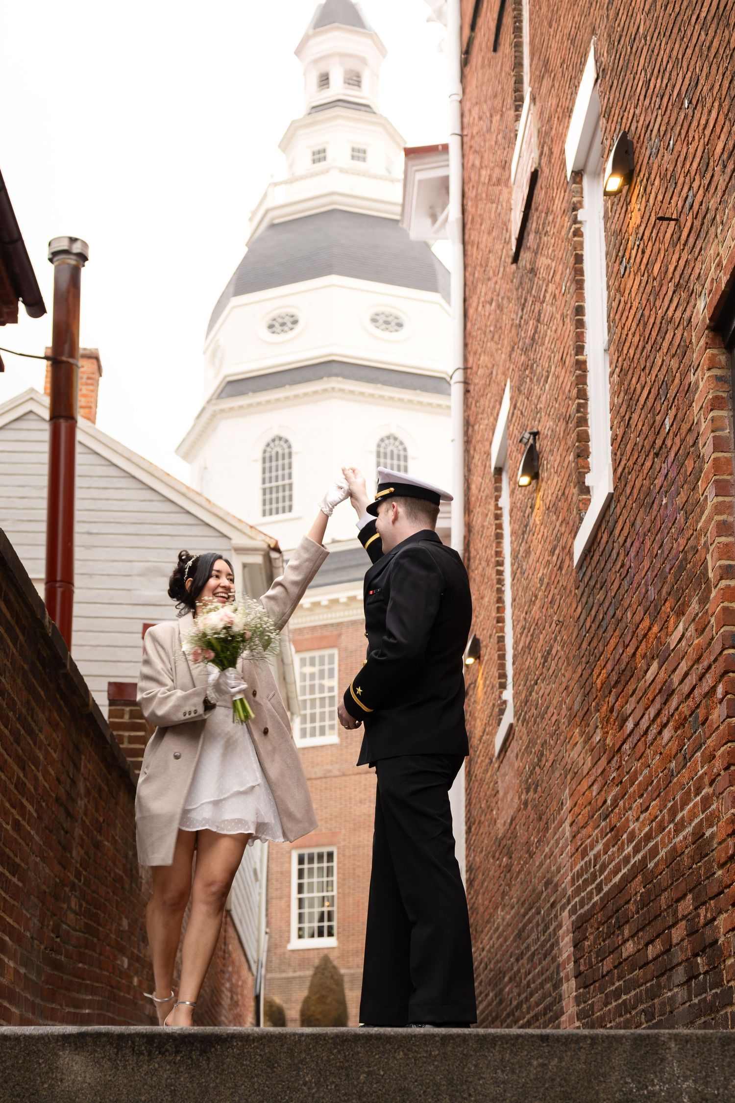 Couple shares romantic moment on brick steps with historic domed building in background.