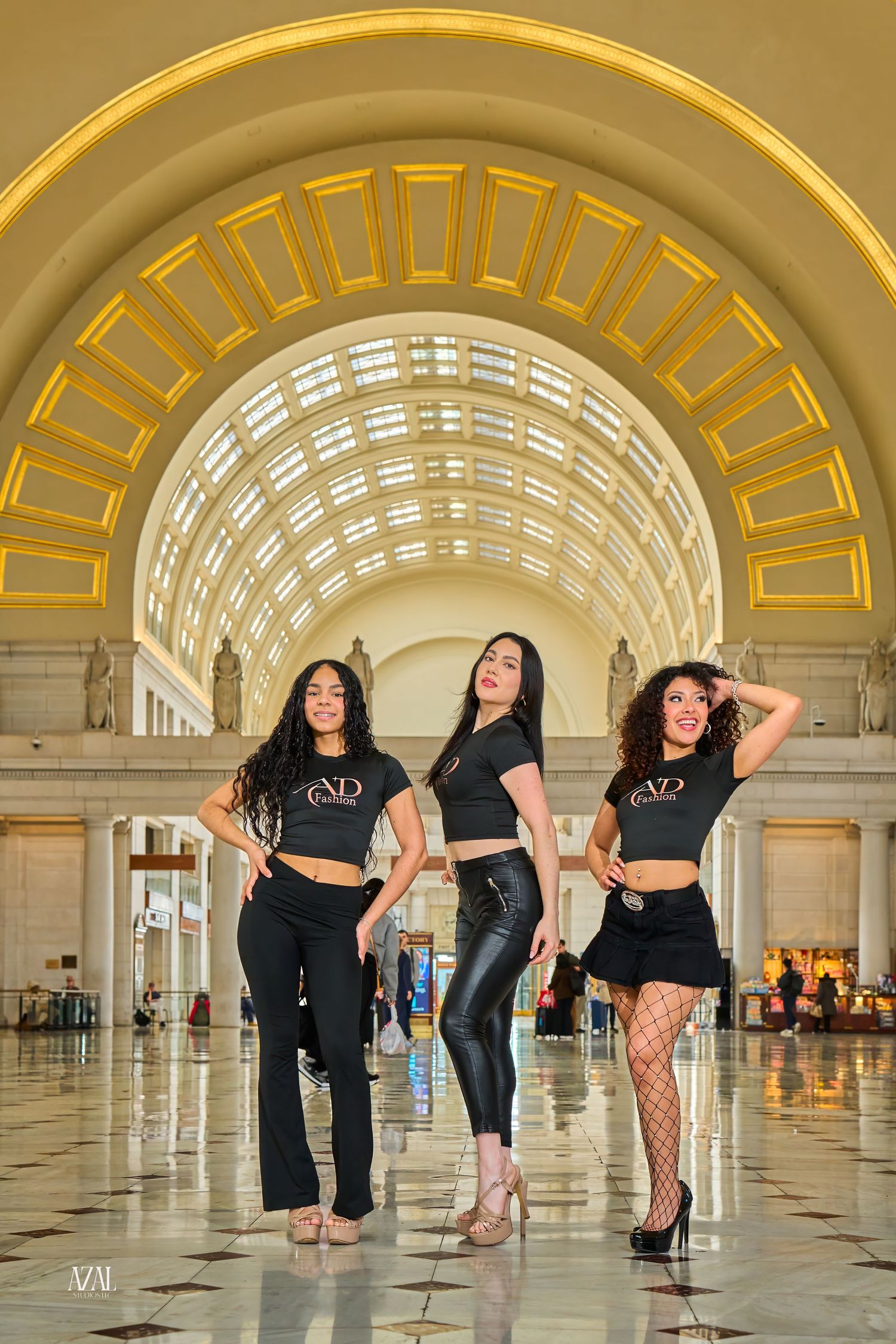 Three women in matching black VD Fashion outfits pose together in Union Station's grand arched hall.