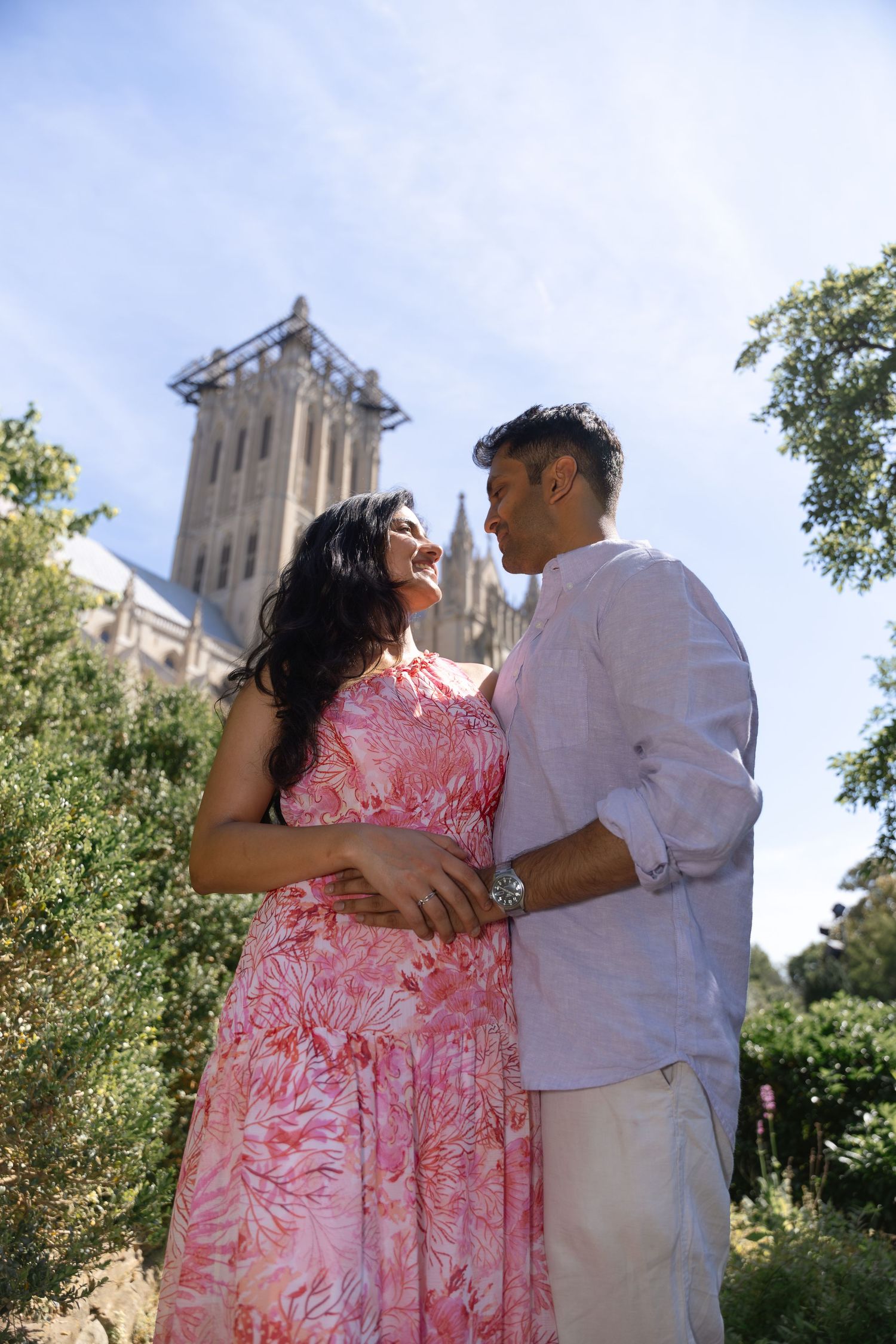 A couple share an intimate moment in front of a church building on a sunny day.