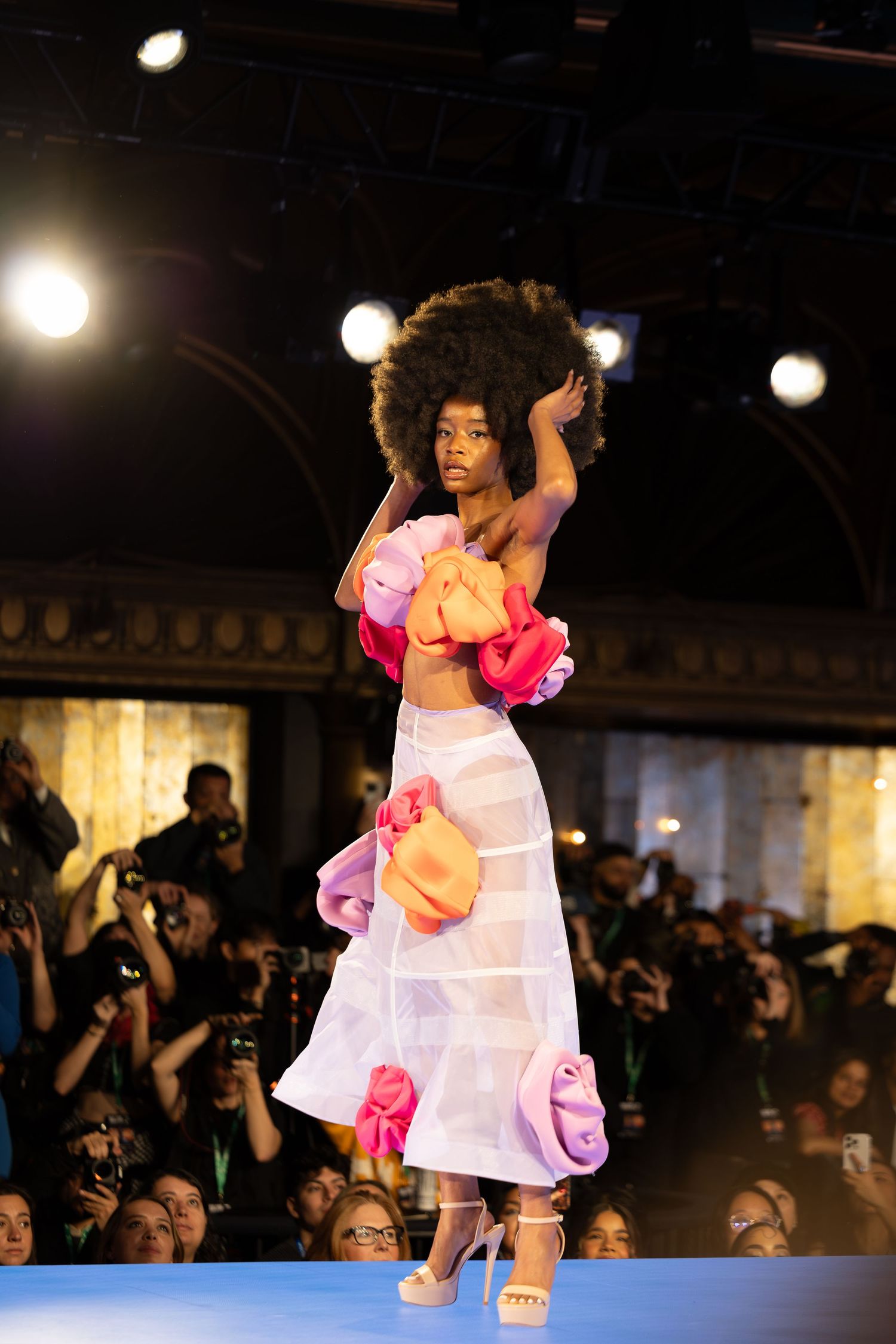Model walks runway in white and pink floral dress with ruffled details.