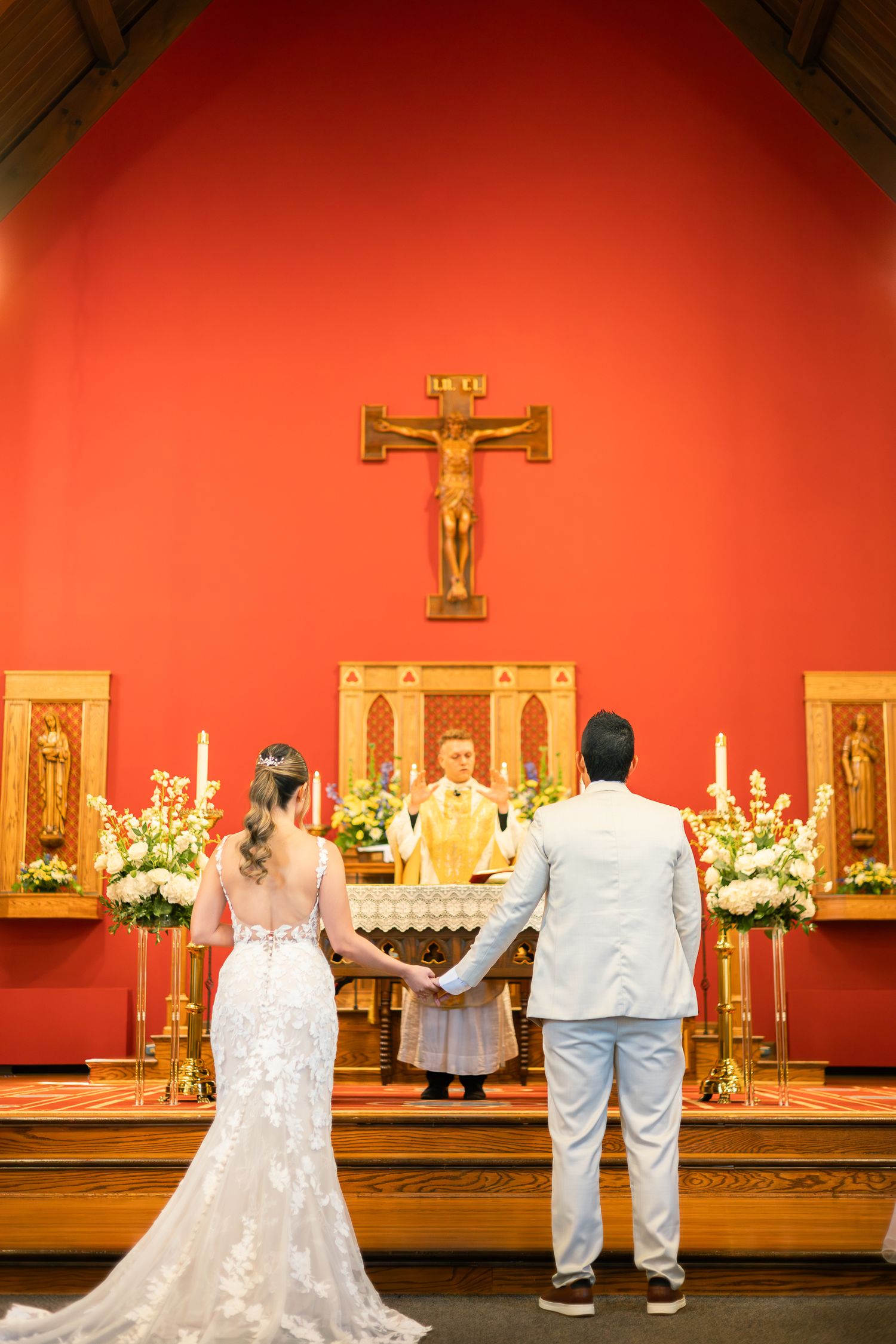 Wedding ceremony setup with red walls and crucifix at altar featuring white floral arrangements.