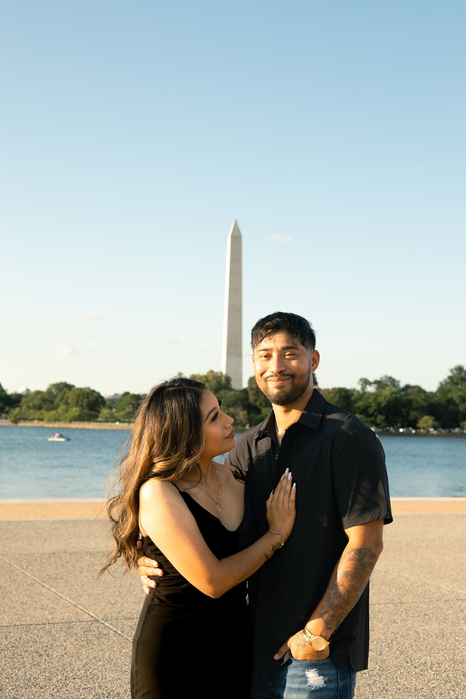 A couple shares a romantic moment together at sunset with the Washington Monument visible in the background.