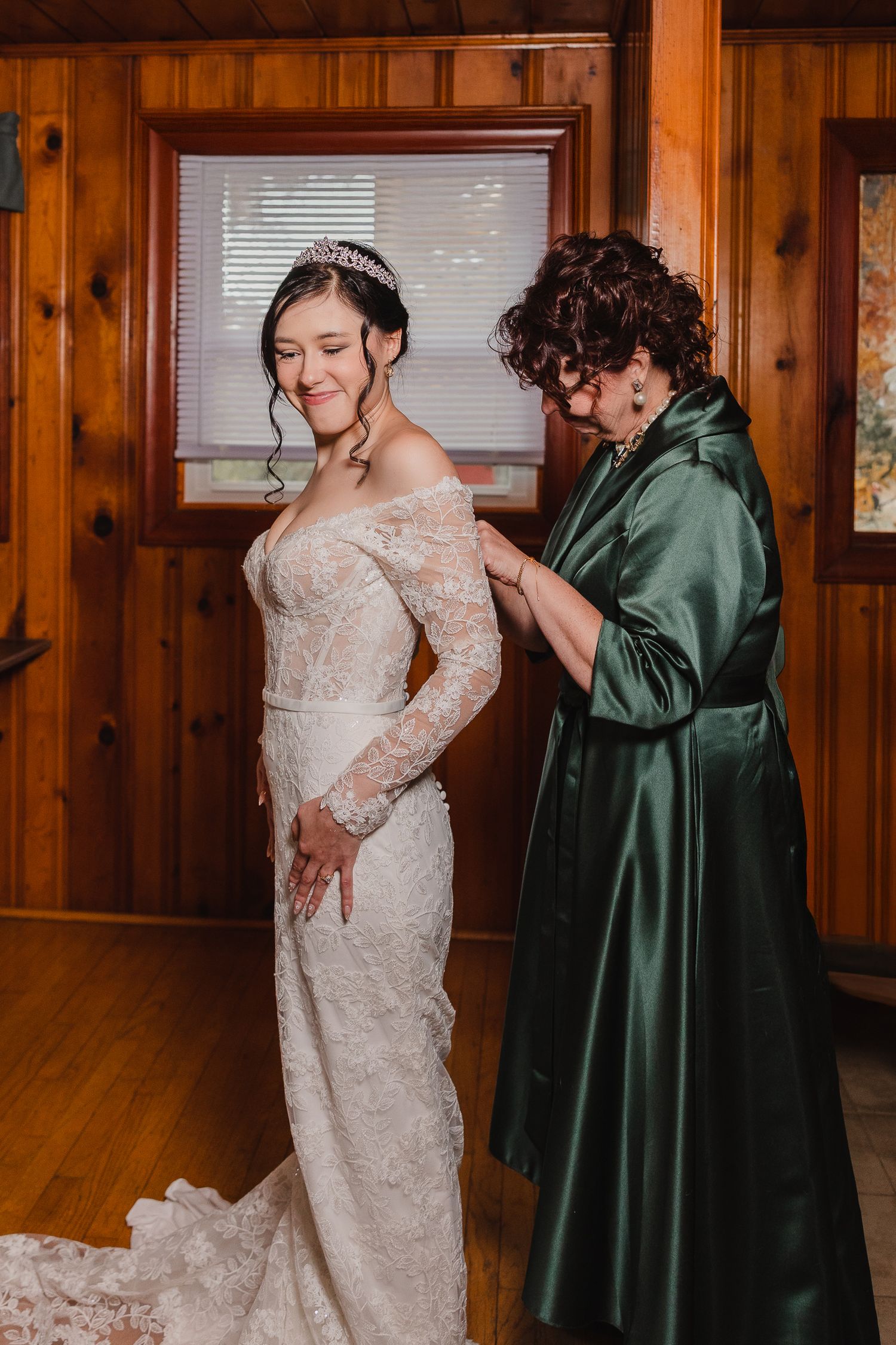 A touching moment of getting dressed in a white lace wedding gown with someone in a dark green robe helping.
