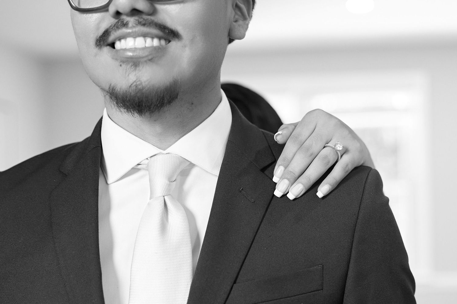 Black and white portrait of someone in a formal suit and tie with a hand resting on their shoulder.