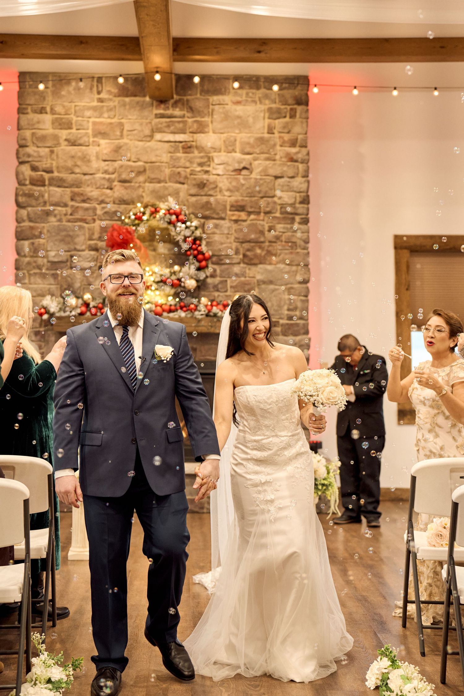 Newlyweds walk down the aisle while guests celebrate in a stone-walled ceremony venue.