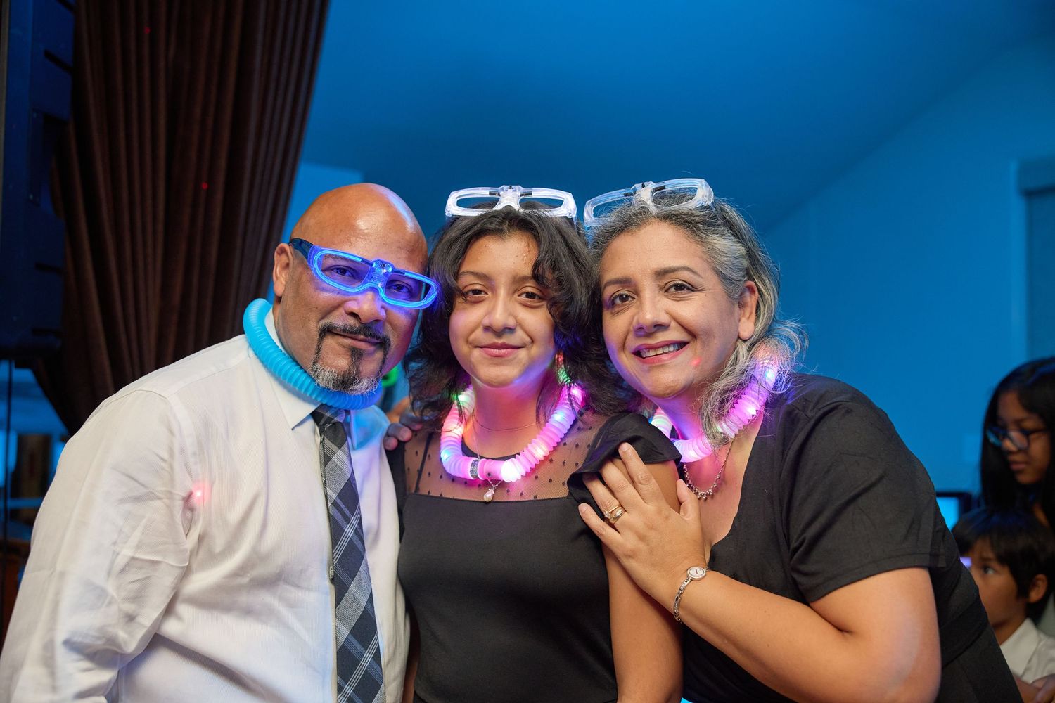 Wedding guests laugh and smile together during a reception celebration with blue lighting and dark curtains in background.