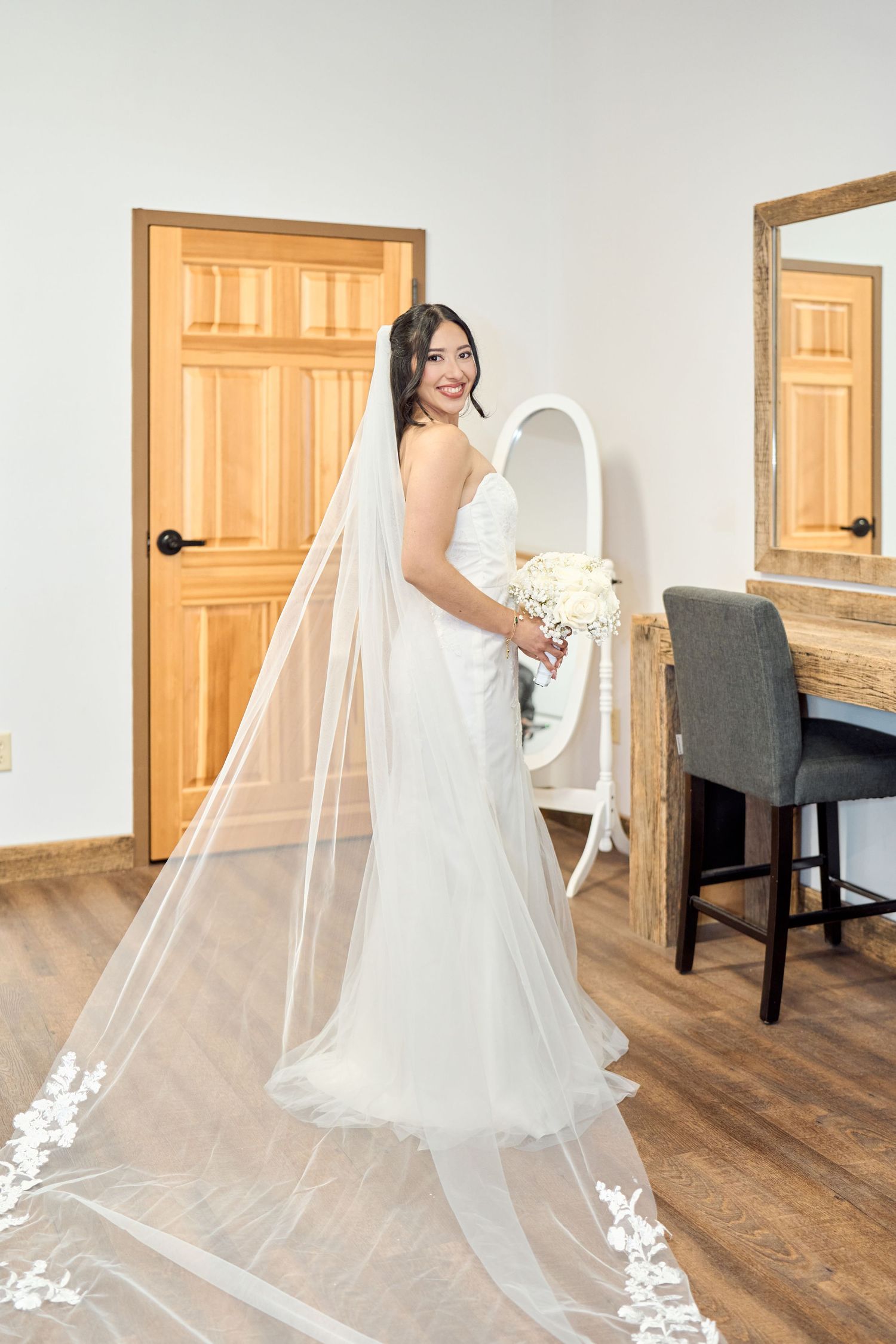 A bride poses in a flowing white wedding gown with a long veil against wooden doors.