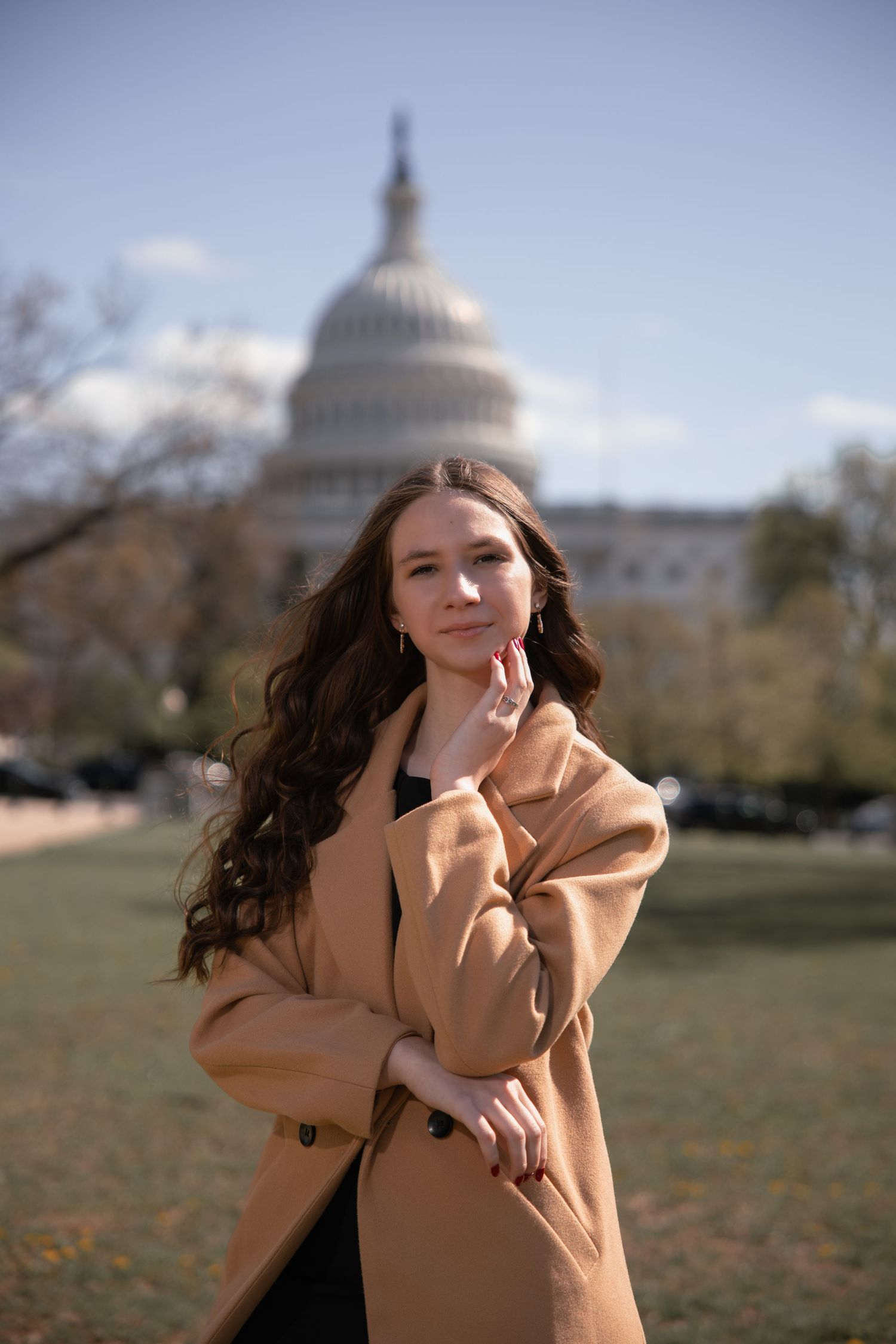 Someone in a tan coat poses on the National Mall with the US Capitol dome visible in the background.
