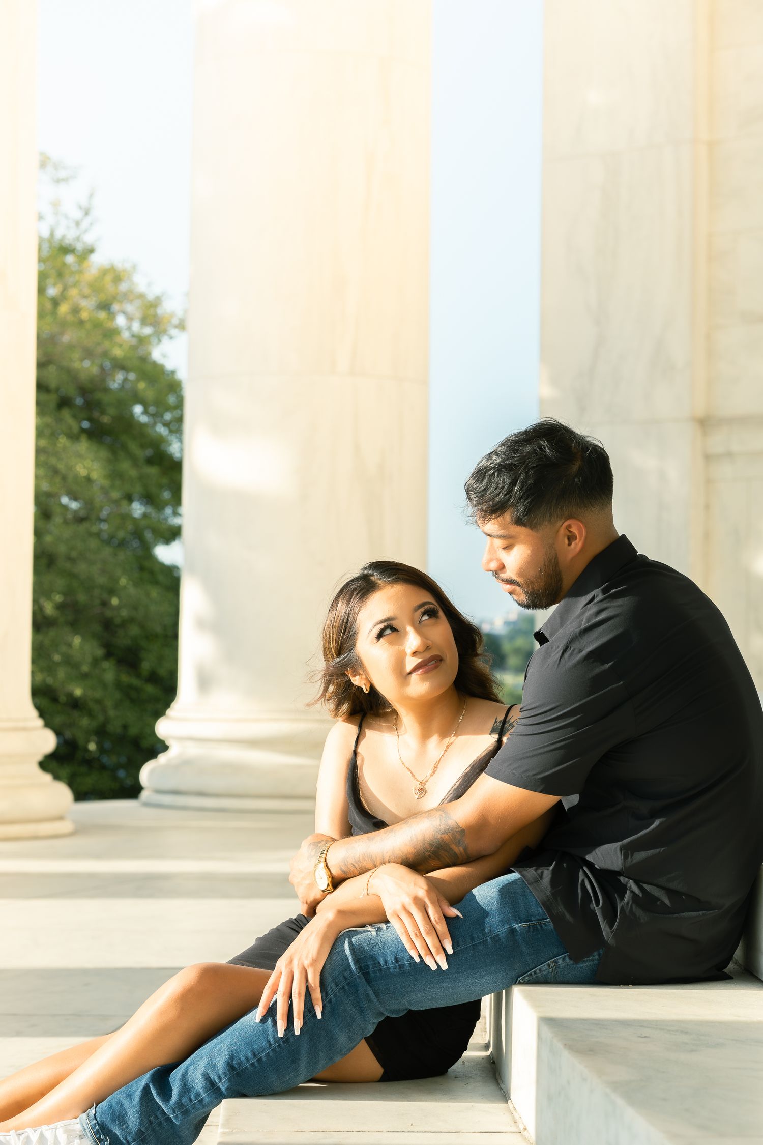 A couple sits intimately together on white marble steps in a romantic outdoor photoshoot series.