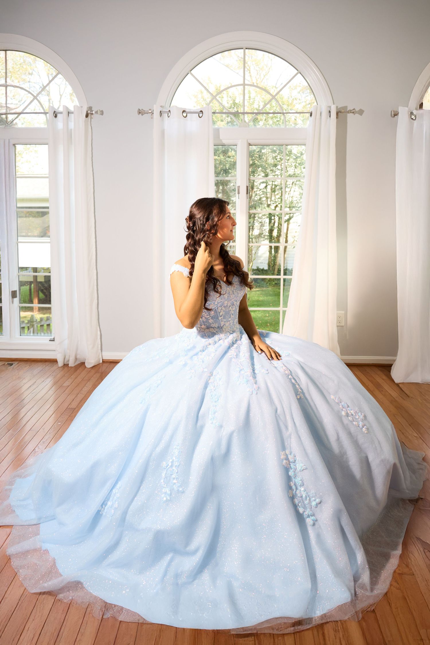 A stunning light blue ballgown with intricate details is showcased in an elegant room with arched windows and hardwood floors.