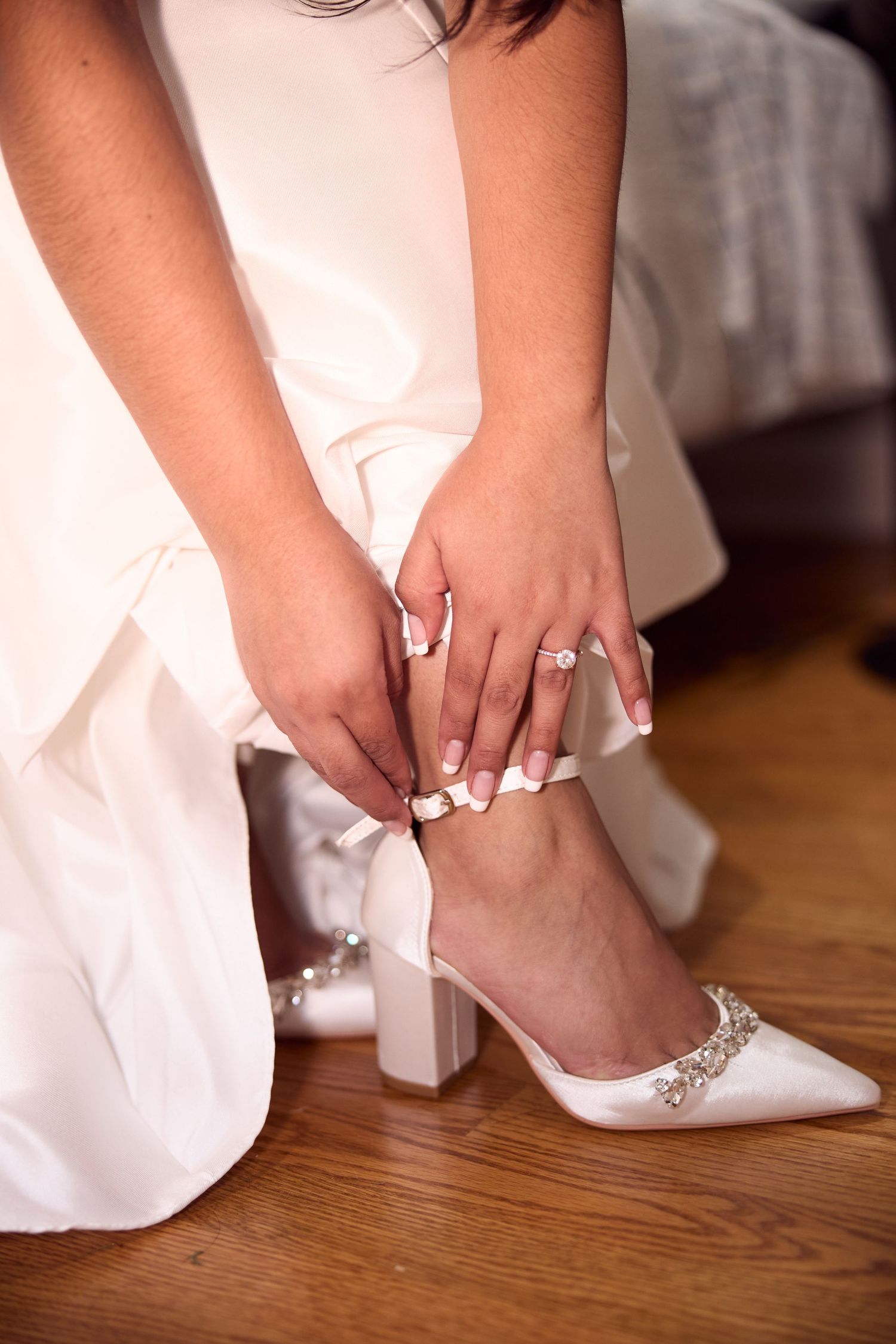 Close-up sequence showing a bride putting on elegant white wedding shoes with crystal details on hardwood floor.