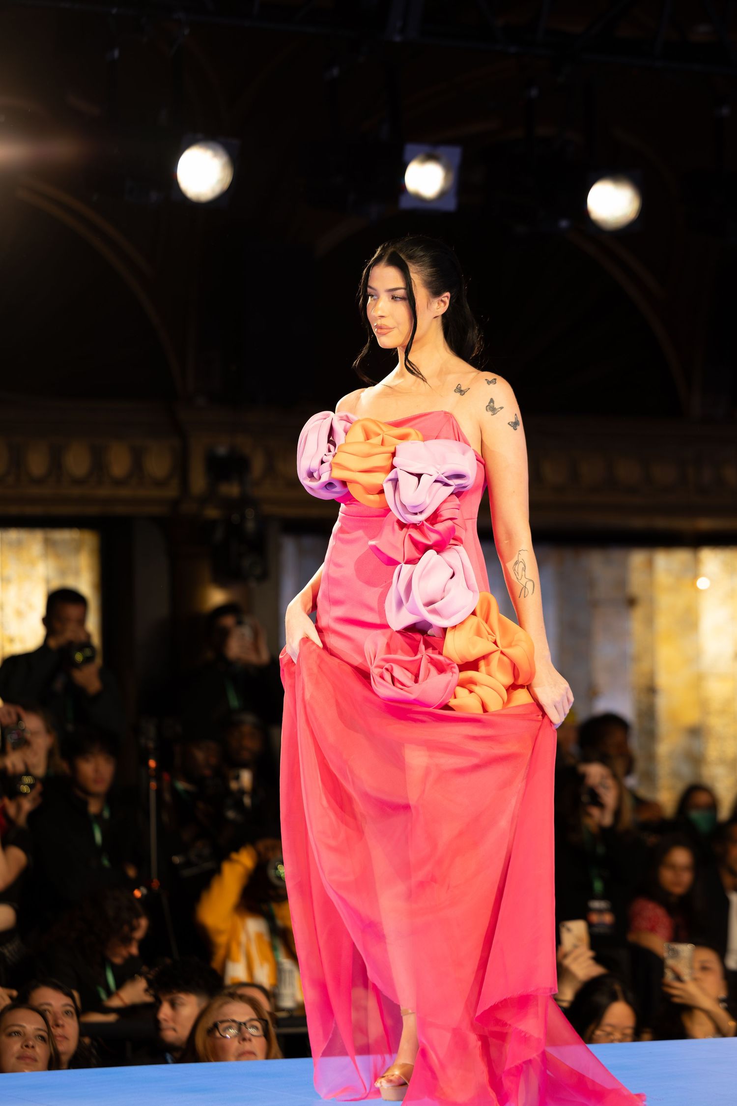 Model presents pink evening gown with floral details during fashion show.