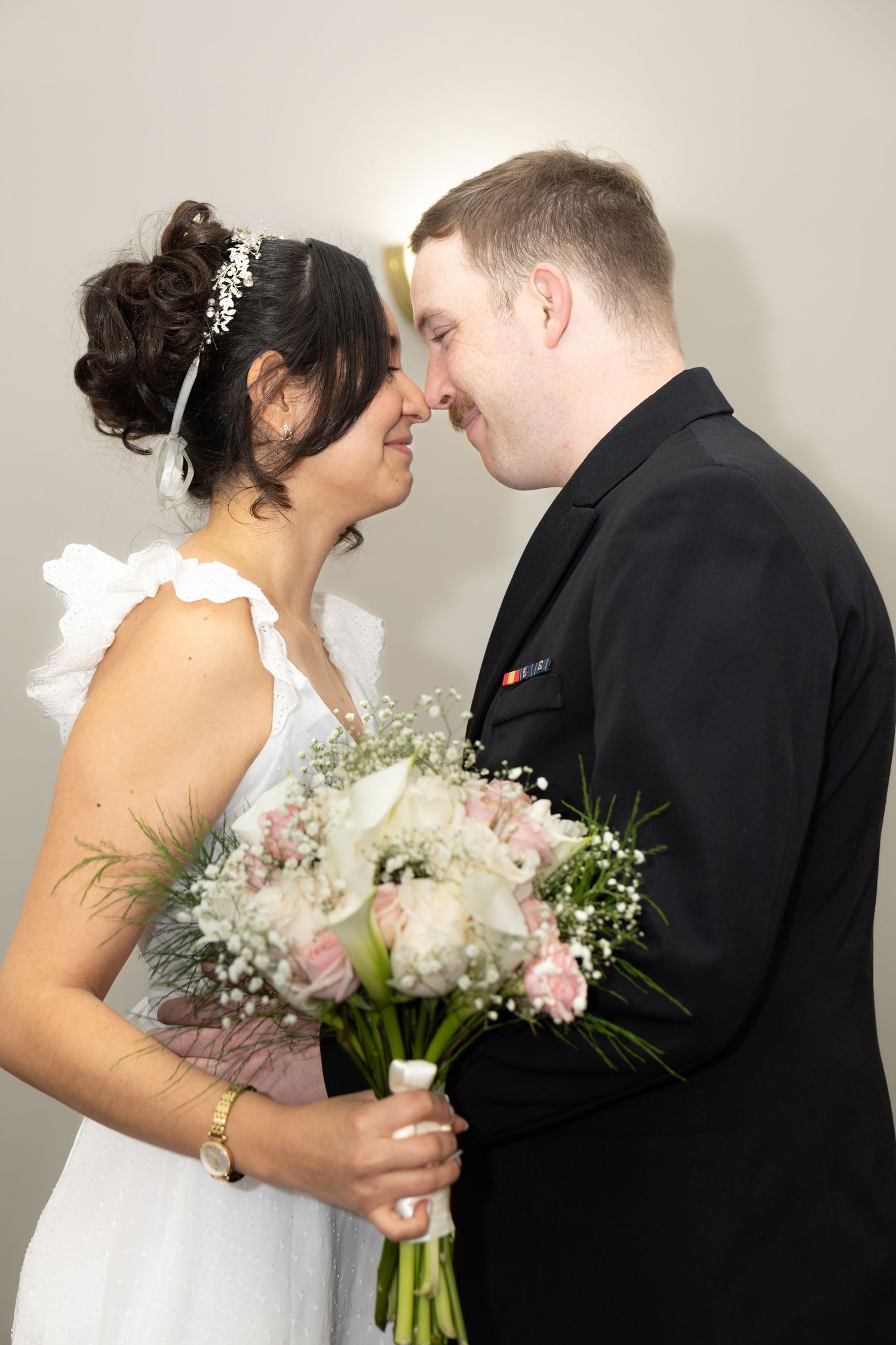 Newlyweds share intimate moment while holding delicate floral bouquet.