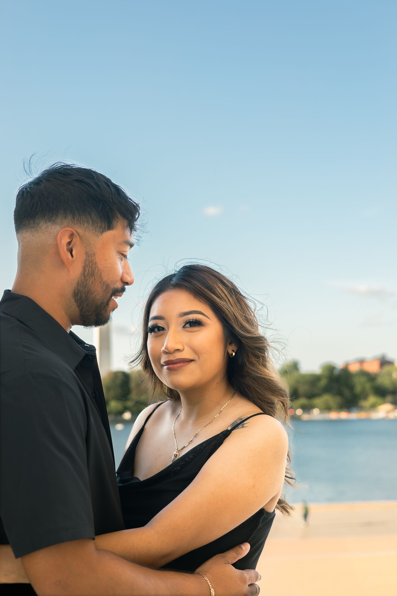 A romantic couple embraces on a beach with a waterfront view during golden hour.