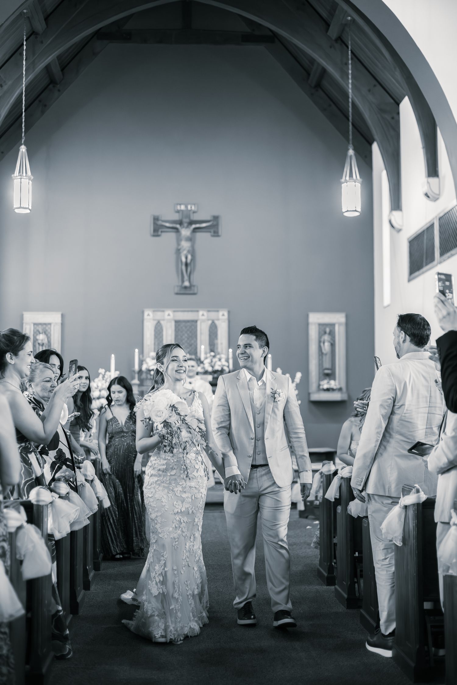 Wedding guests in formal attire gather inside an elegant church with arched ceilings and white walls.