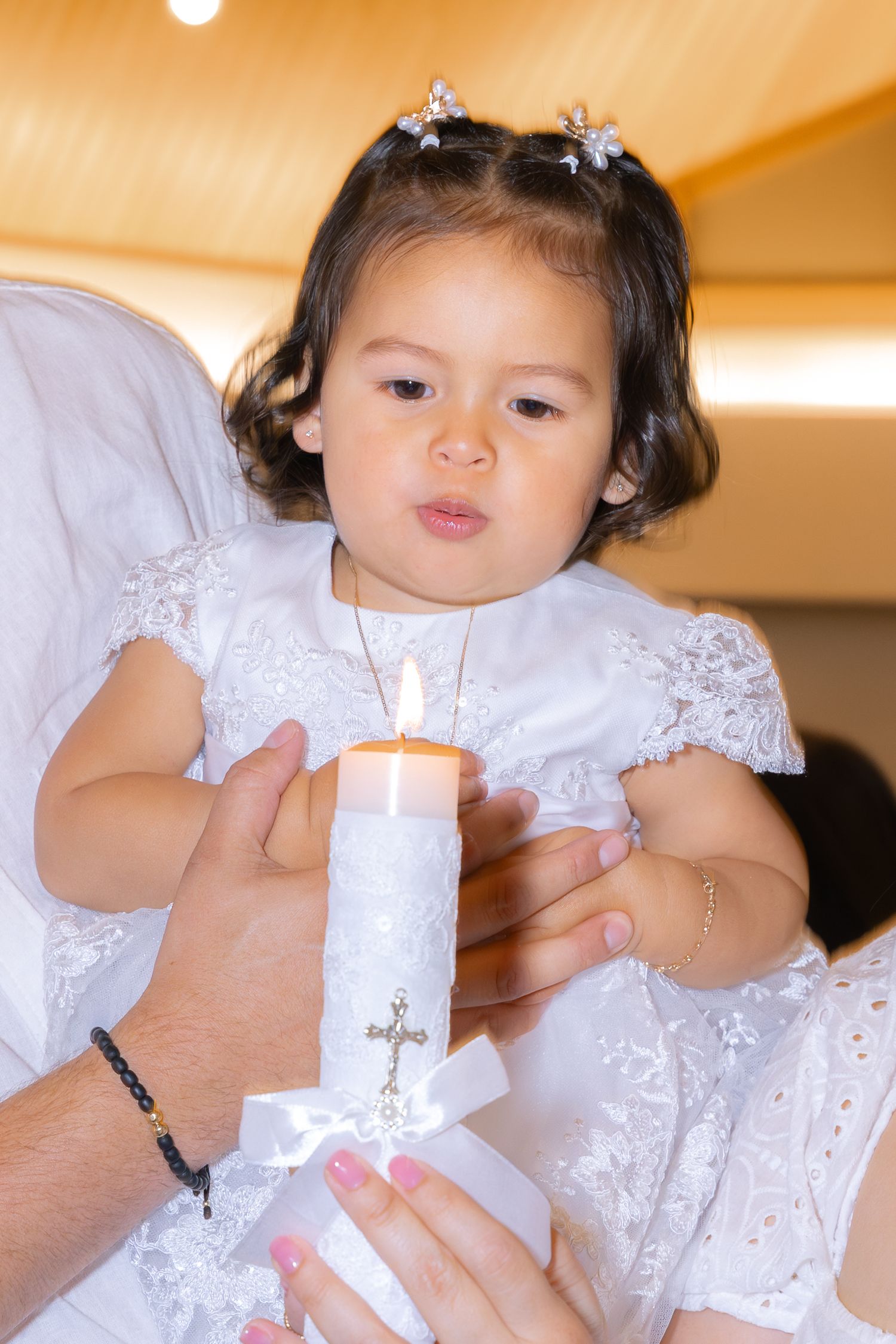 A young child wearing a white lace dress participates in a candle ceremony during a religious celebration.