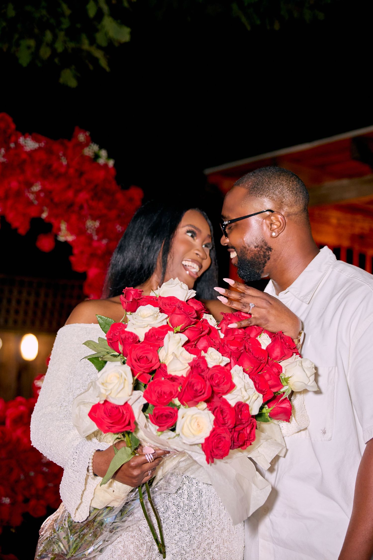 A romantic couple shares tender moments with red and white roses during a nighttime celebration.