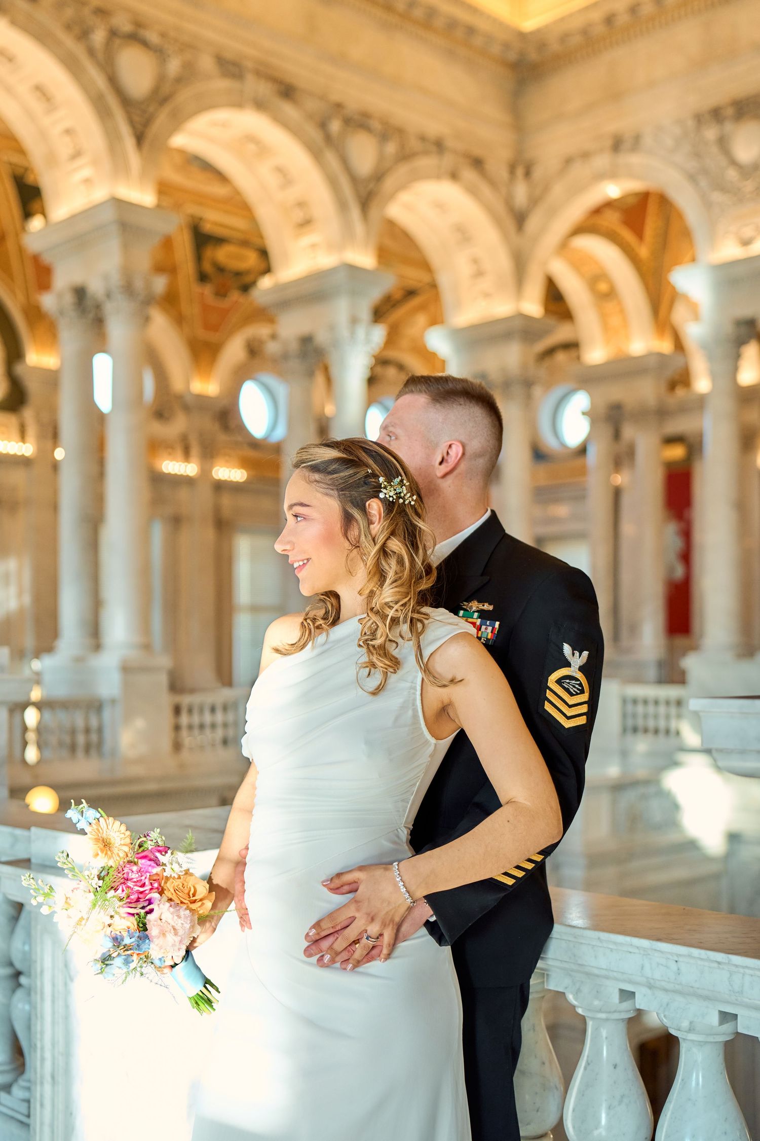 Military groom in dress uniform embraces bride holding colorful bouquet in ornate marble Library of Congress.