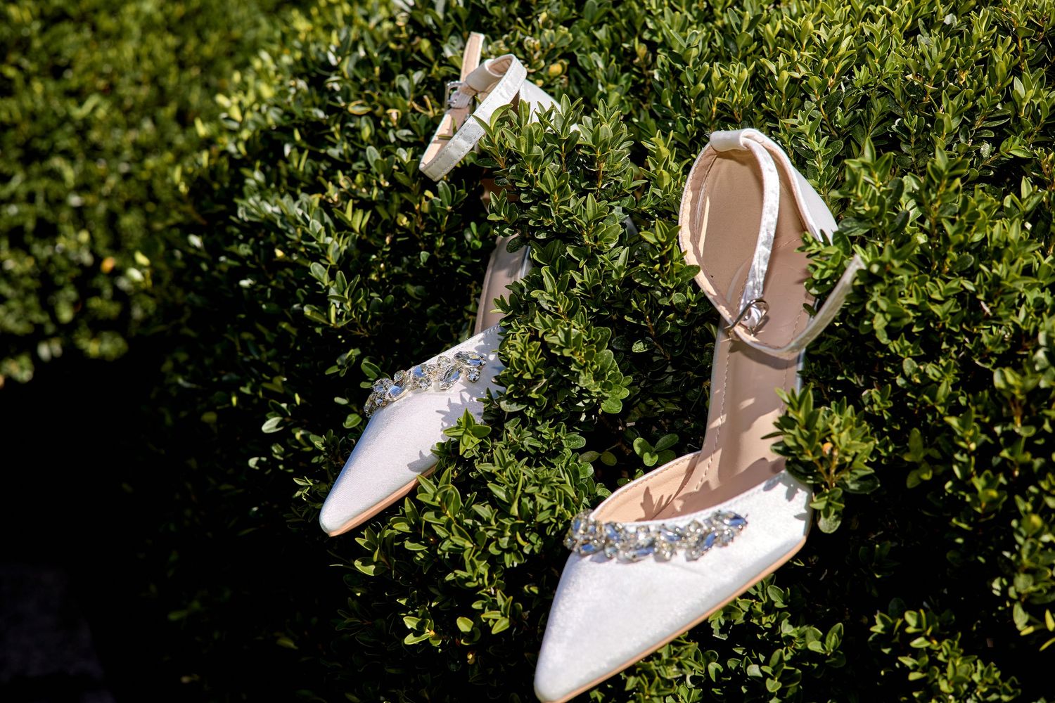 White wedding shoes with floral details displayed against a green leafy background.