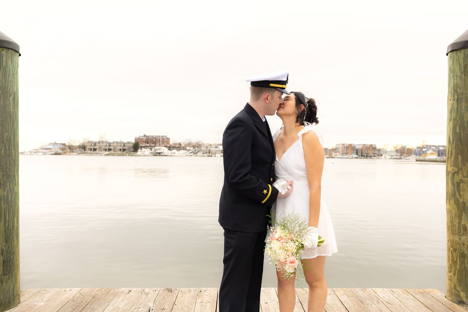 Couple shares intimate moment on wooden pier with waterfront view.