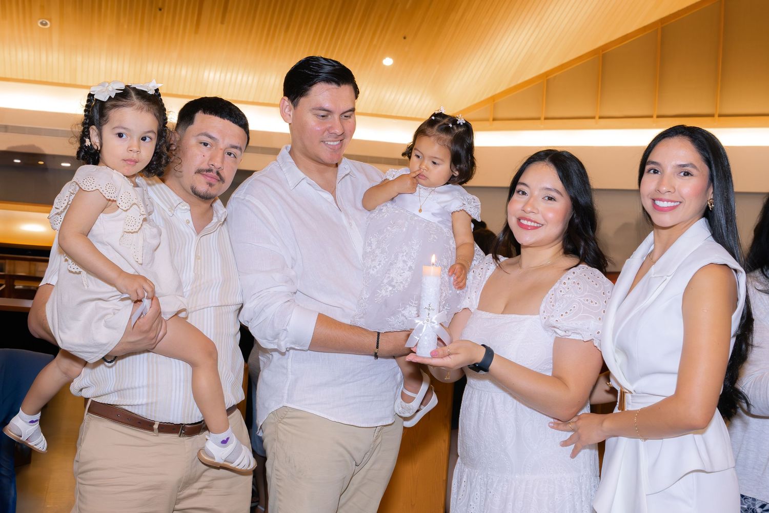 Family group wearing coordinated white and beige outfits posing together in an indoor venue.