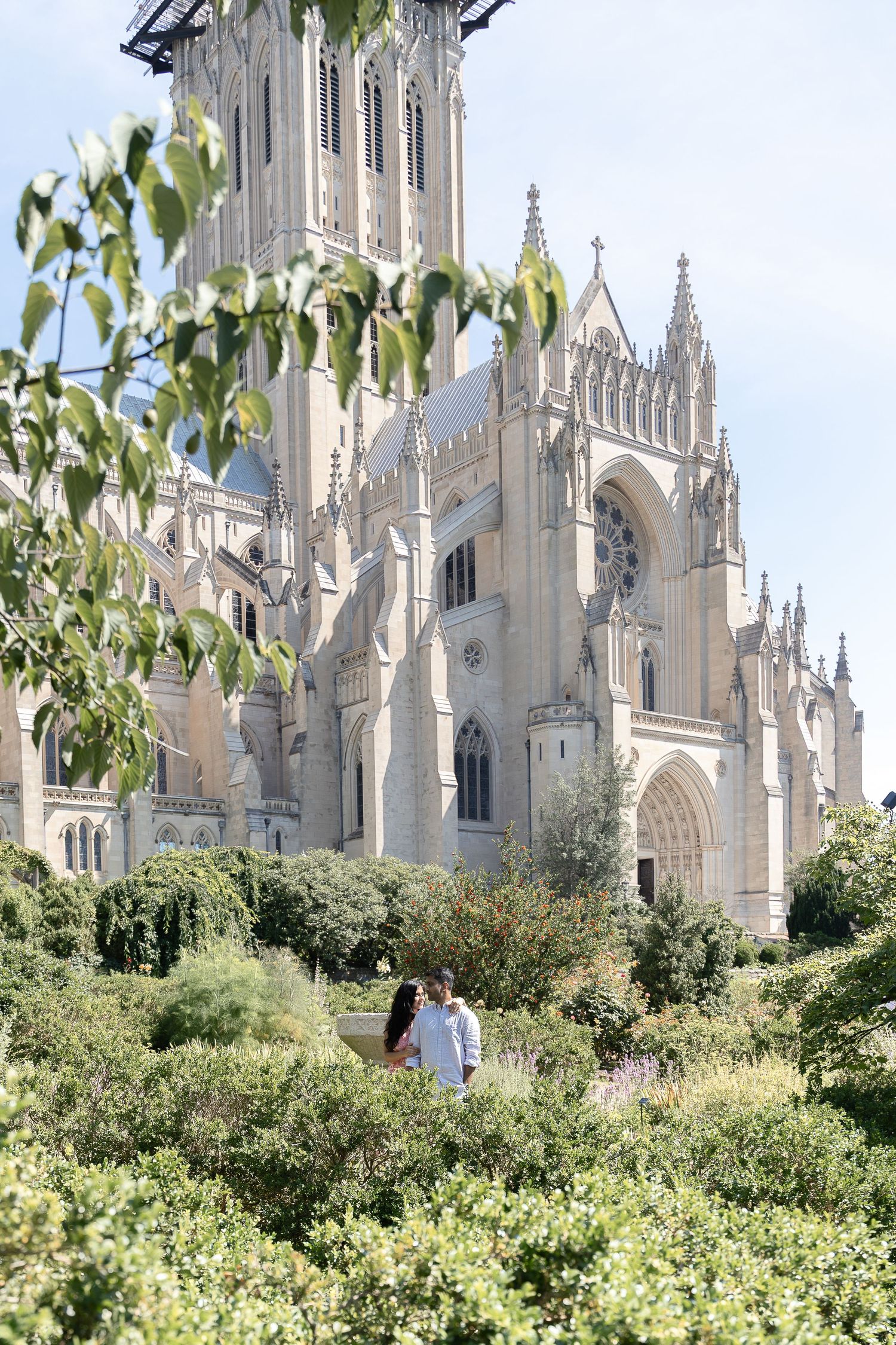 Gothic cathedral spires rise above lush green foliage against a bright sky in Washington National Cathedral.