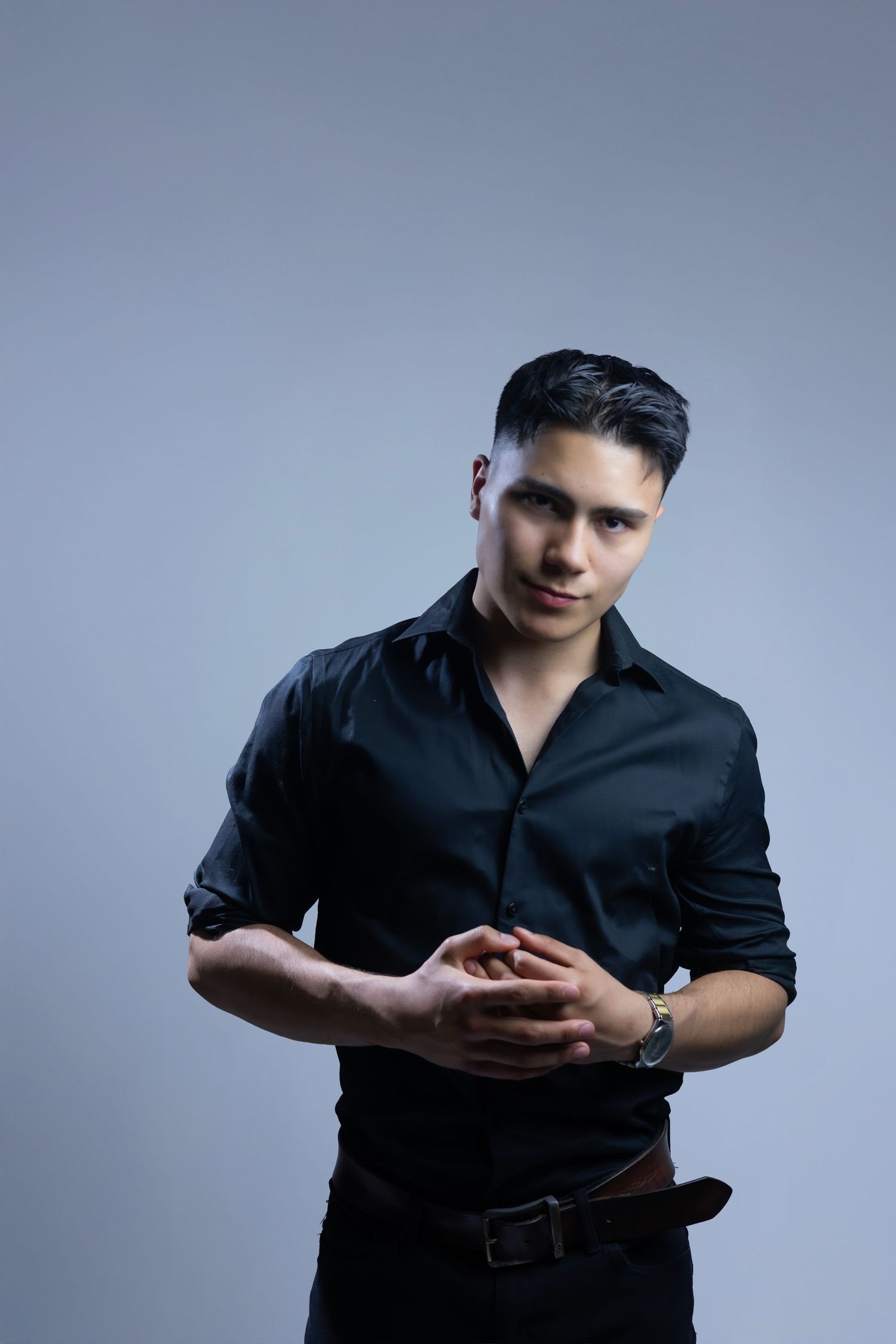 Man in black button-down shirt poses against blue studio background looking at his phone screen.