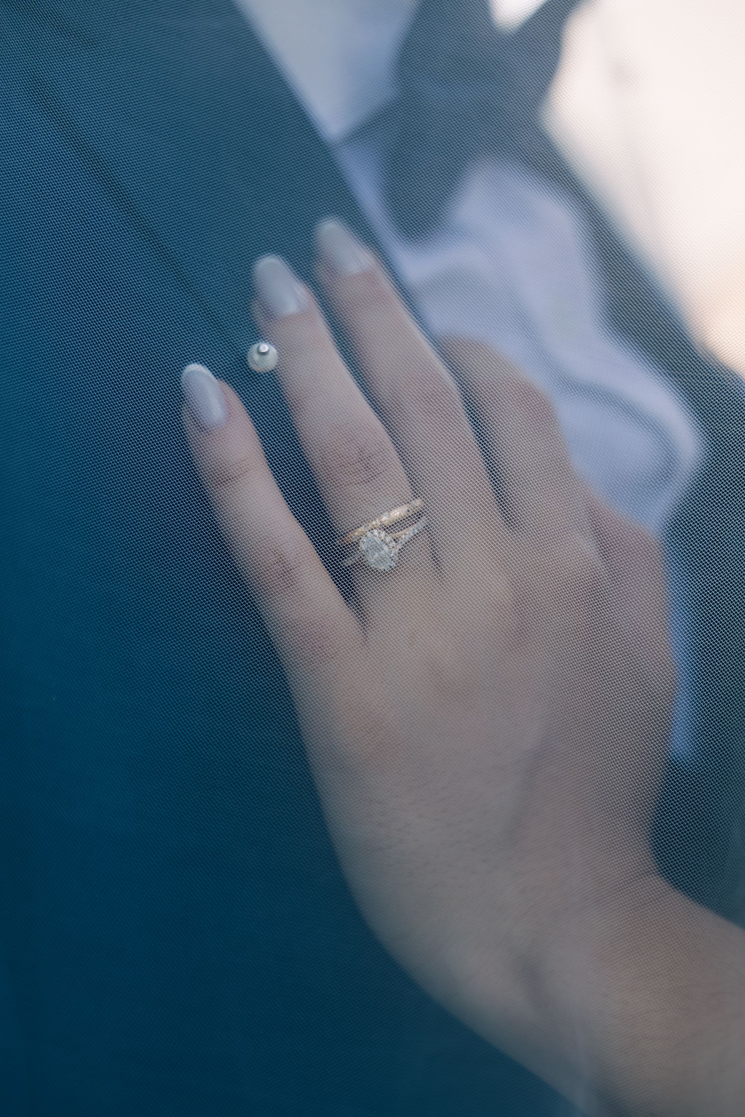 A close-up shot of a hand wearing an elegant diamond engagement ring against a dark blue background.
