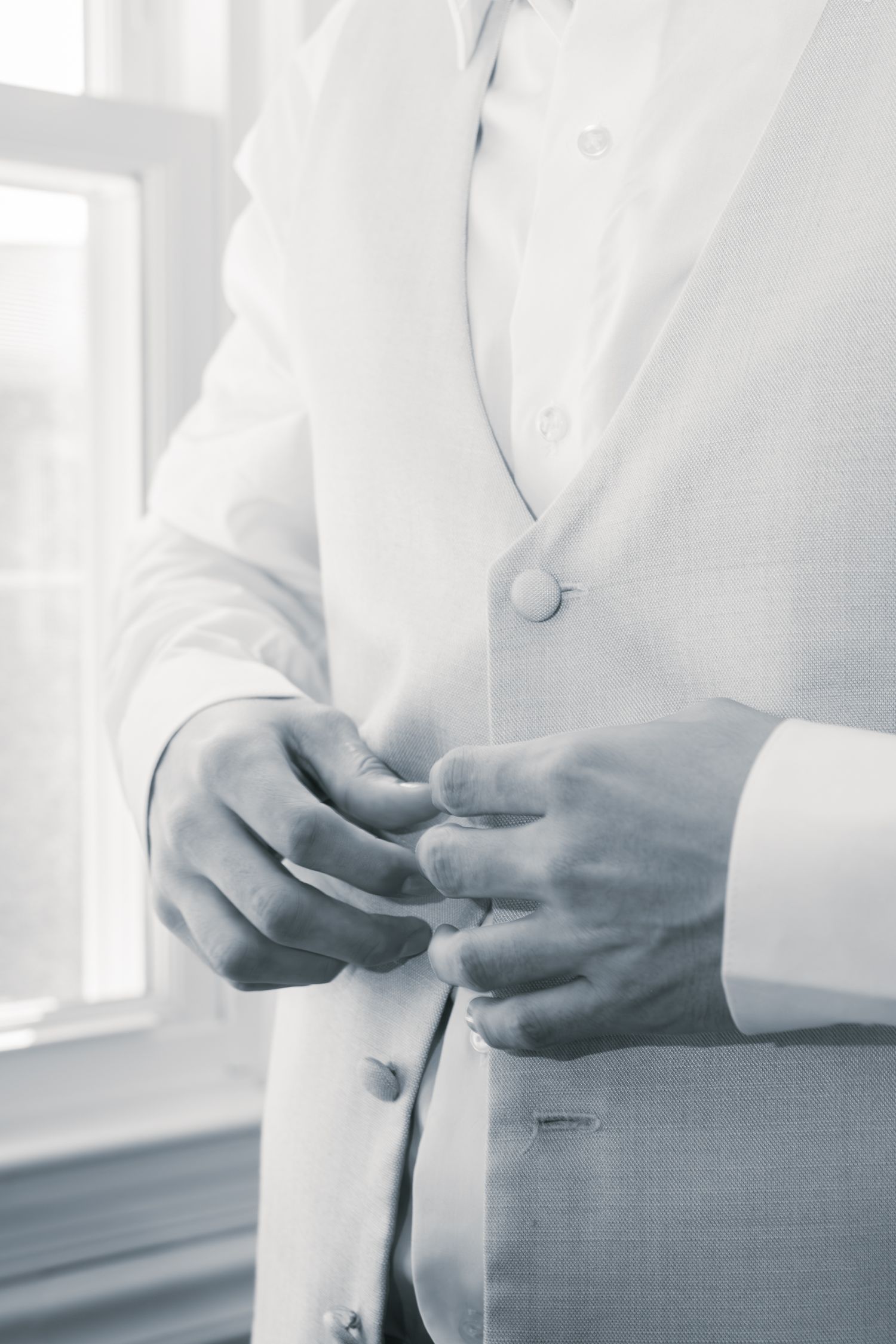 Close-up view of hands adjusting buttons on a white formal suit jacket in soft natural lighting.