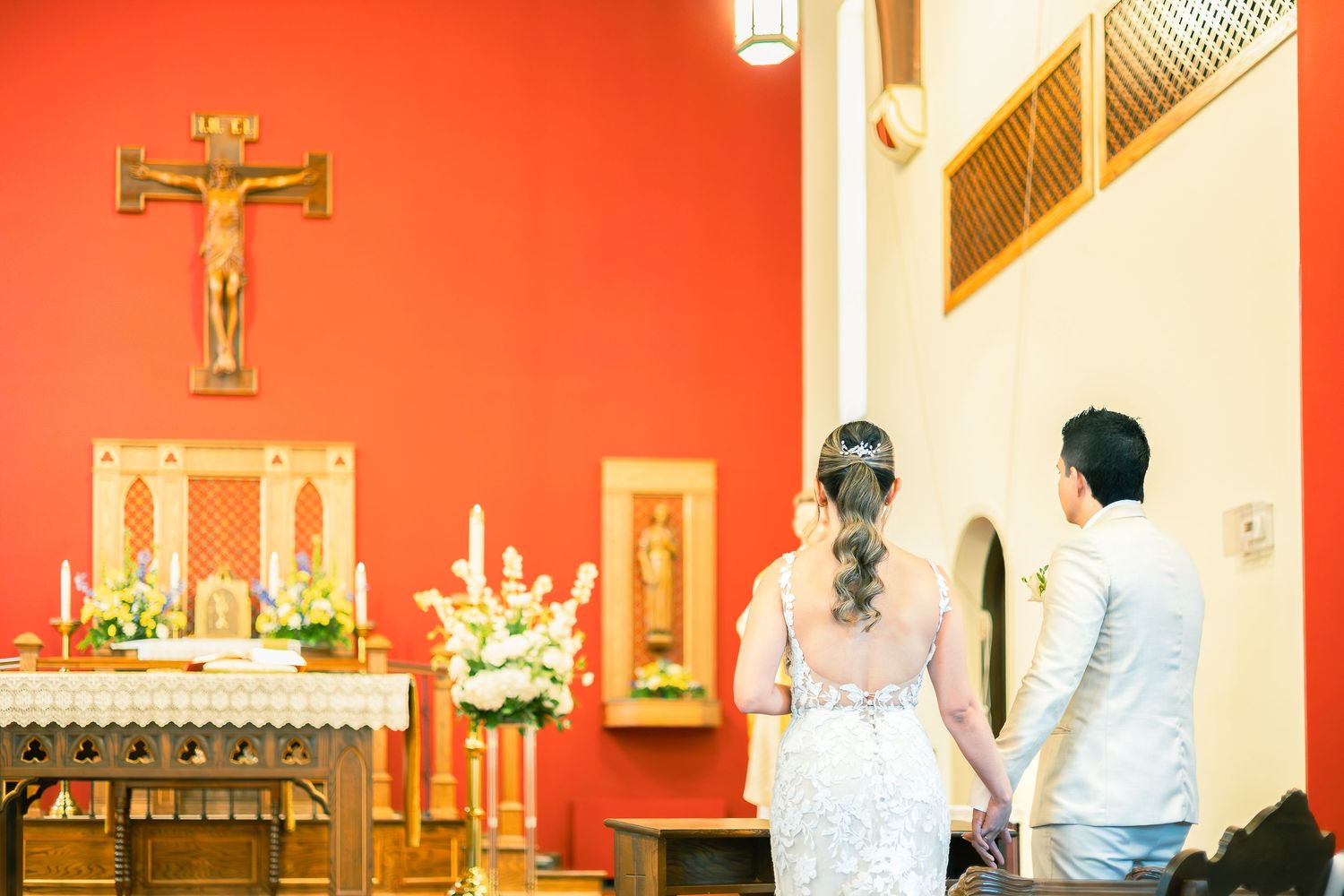 Interior of a church sanctuary with red walls, wooden pews, and ornate religious decorations.