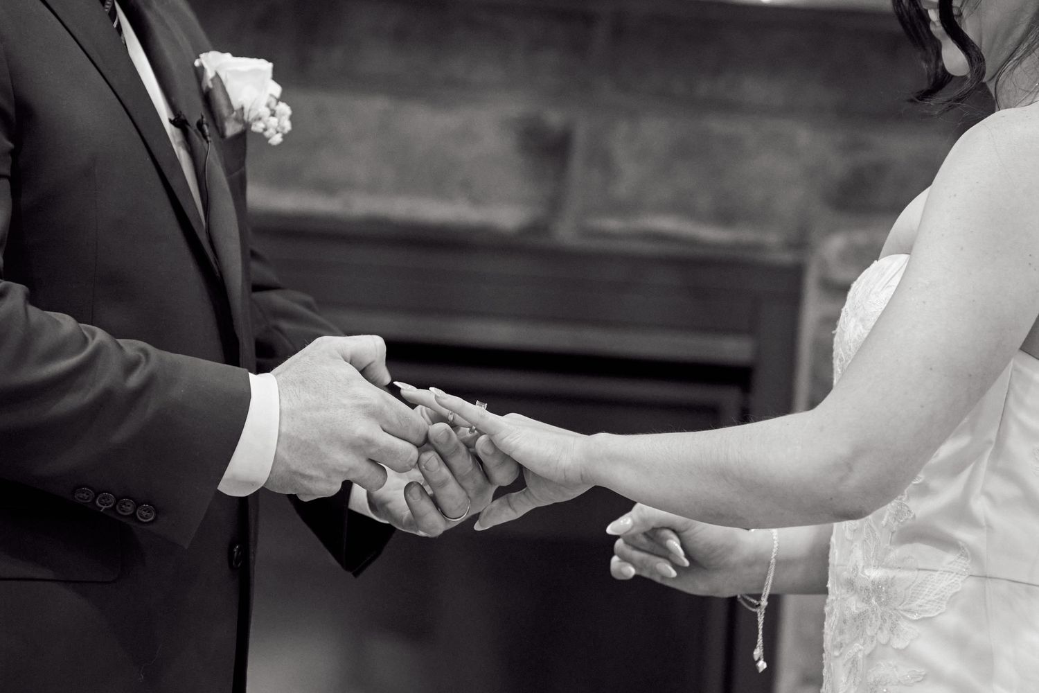Close up of two hands exchanging wedding rings during an outdoor ceremony.