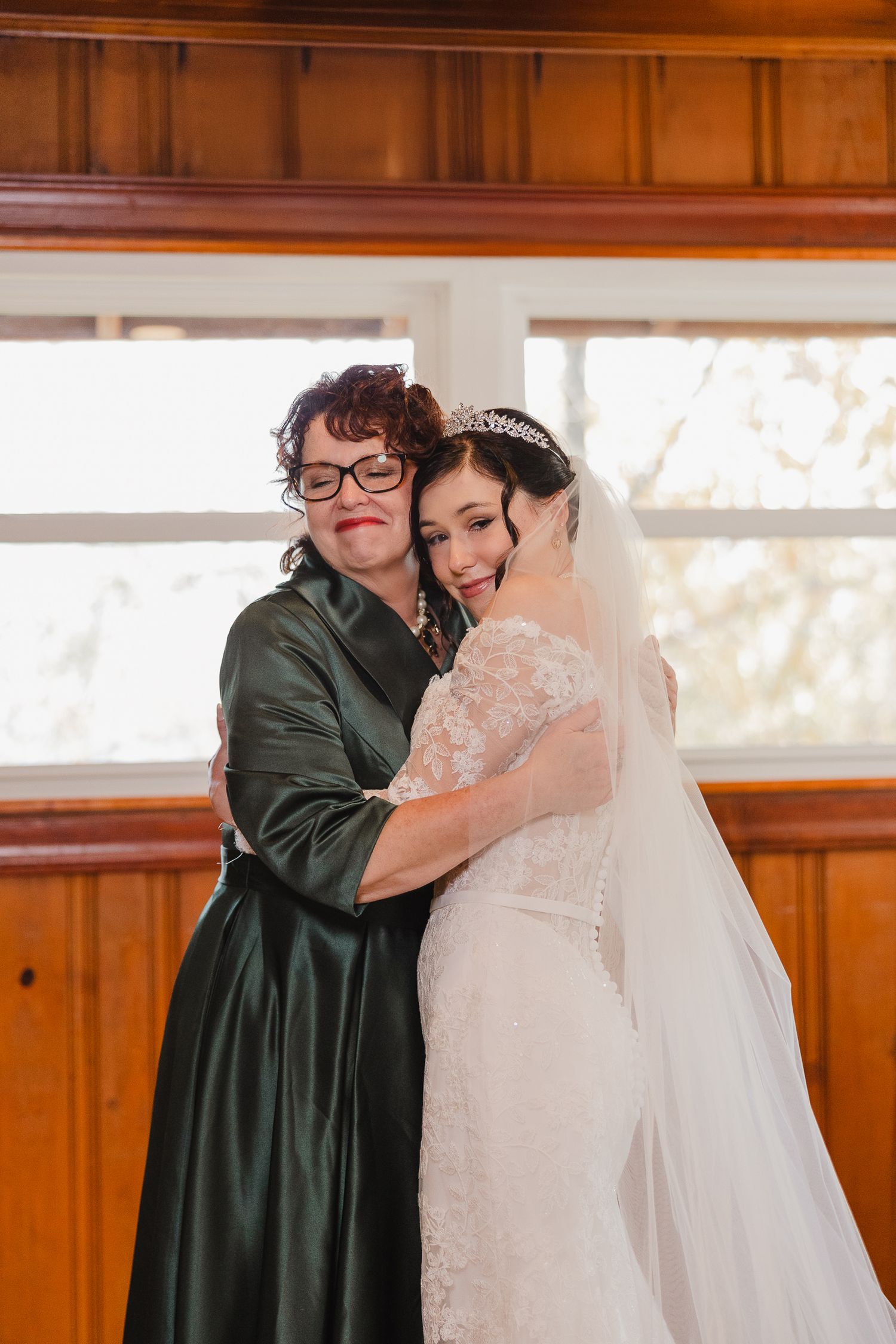 An emotional wedding preparation moment between two people in a wood-paneled room.