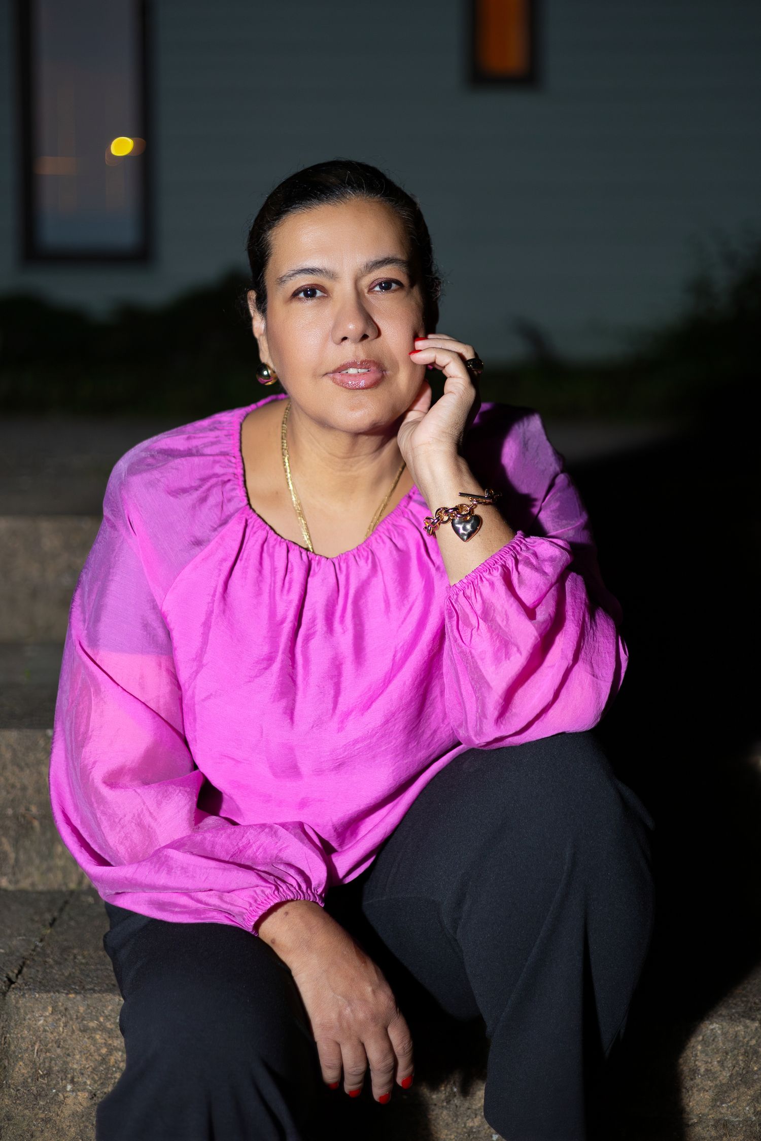 Person in bright pink blouse and dark pants poses against dark background in artistic photo series.