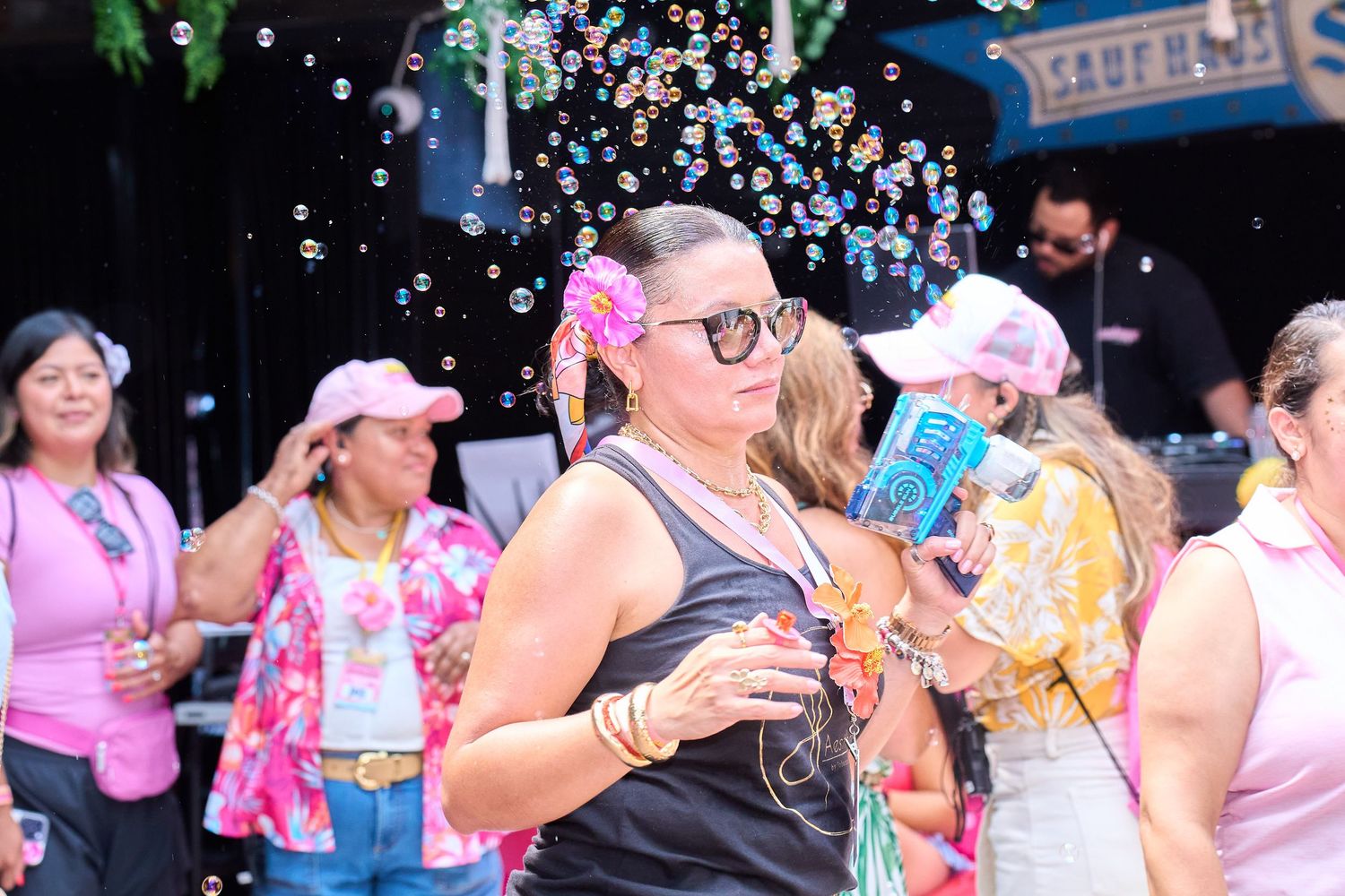 Woman blowing bubbles at a vibrant outdoor party with pink-themed decorations and festive crowd.