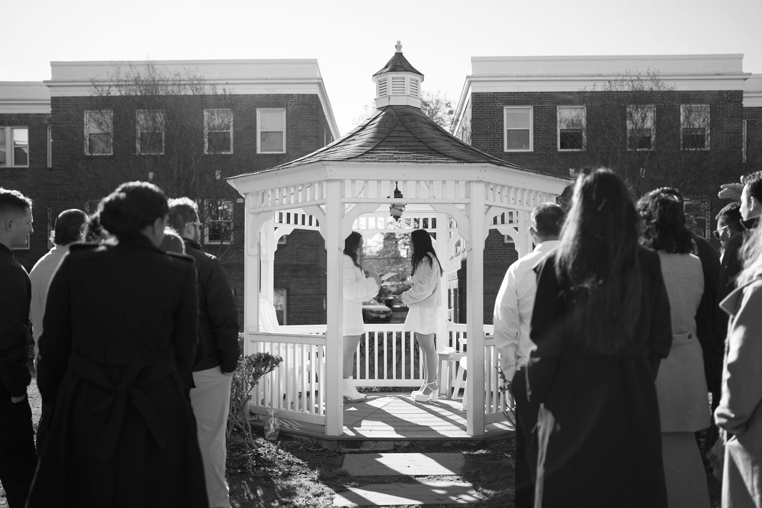 A black and white panoramic photo showing a row of white gazebos and brick buildings in an outdoor setting.